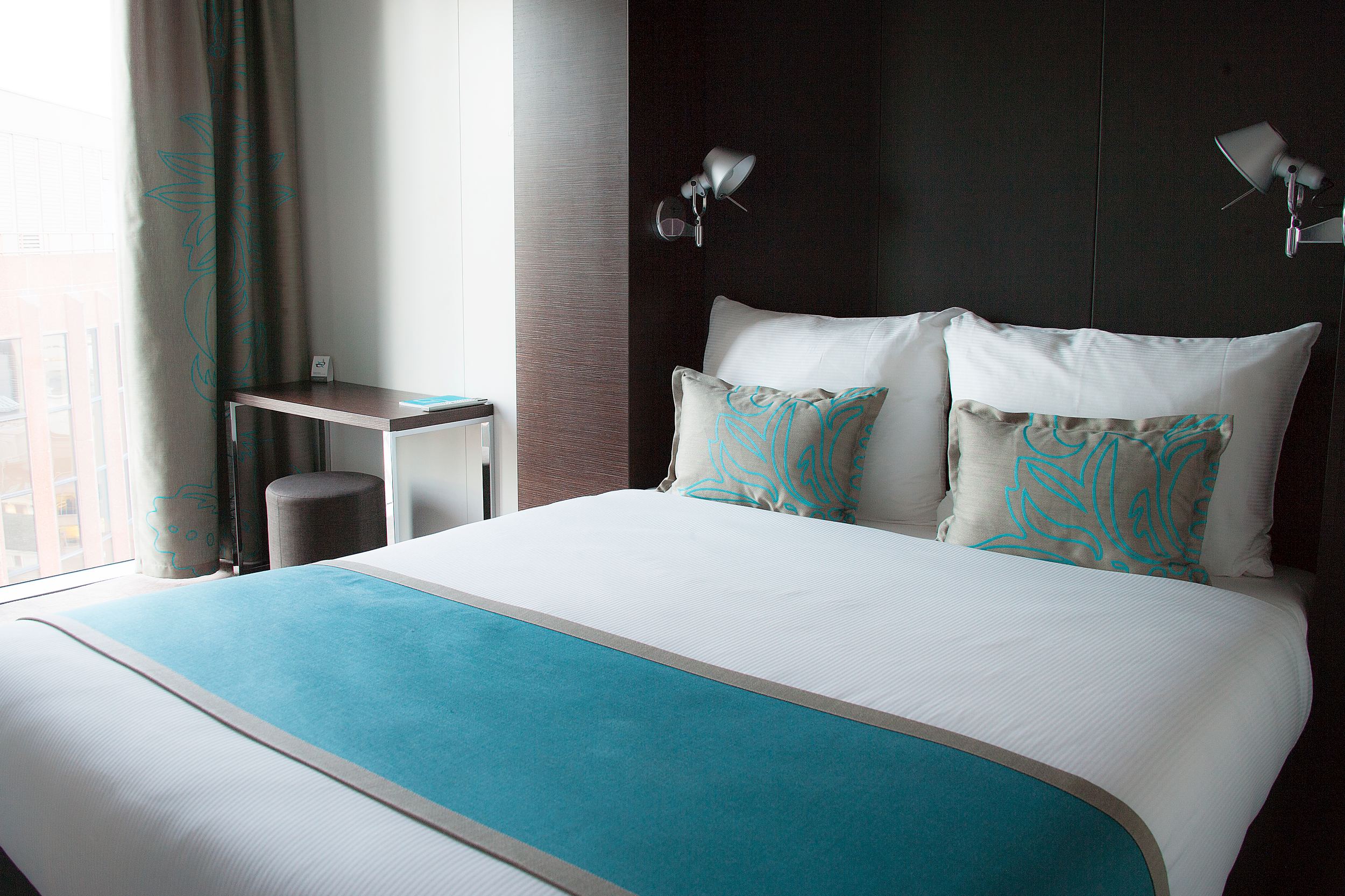 Hotel London Tower Hill Motel One double bed with decorative cushions and small table with stool next to the bed