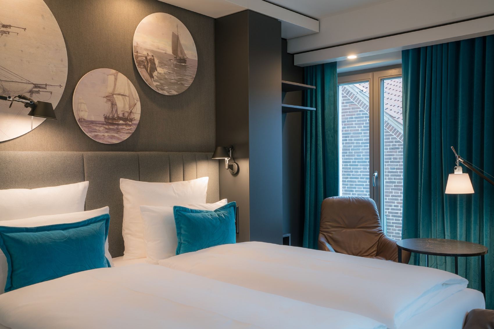 Designhotel Lübeck Motel One geräumiges Doppelbett mit Zierkissen sowie Sessel mit Beistelltisch und Stehlampe