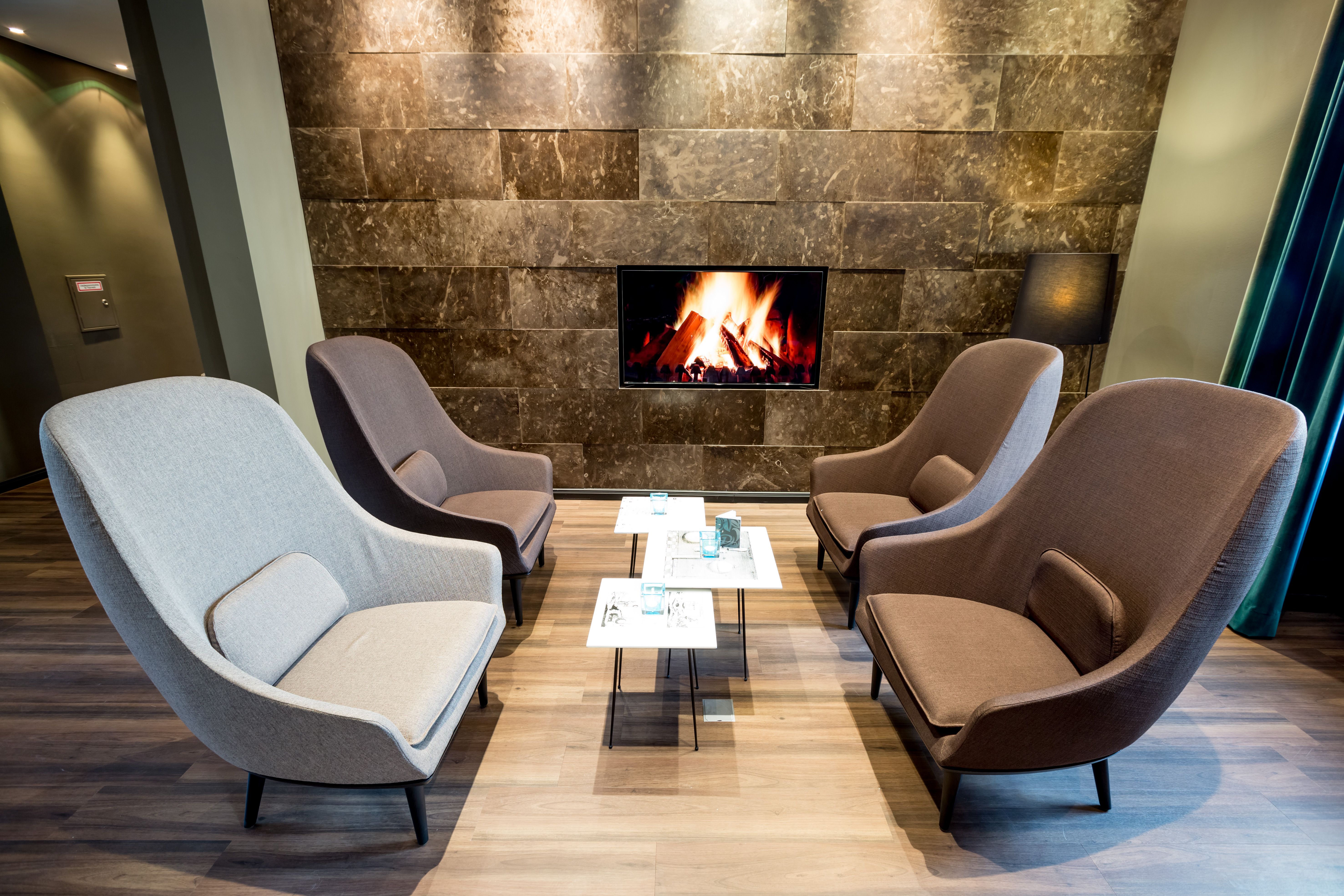 Designhotel Magdeburg Motel One Lounge vier Sessel mit Beistelltischen und Fernseher mit Feuer an der Wand