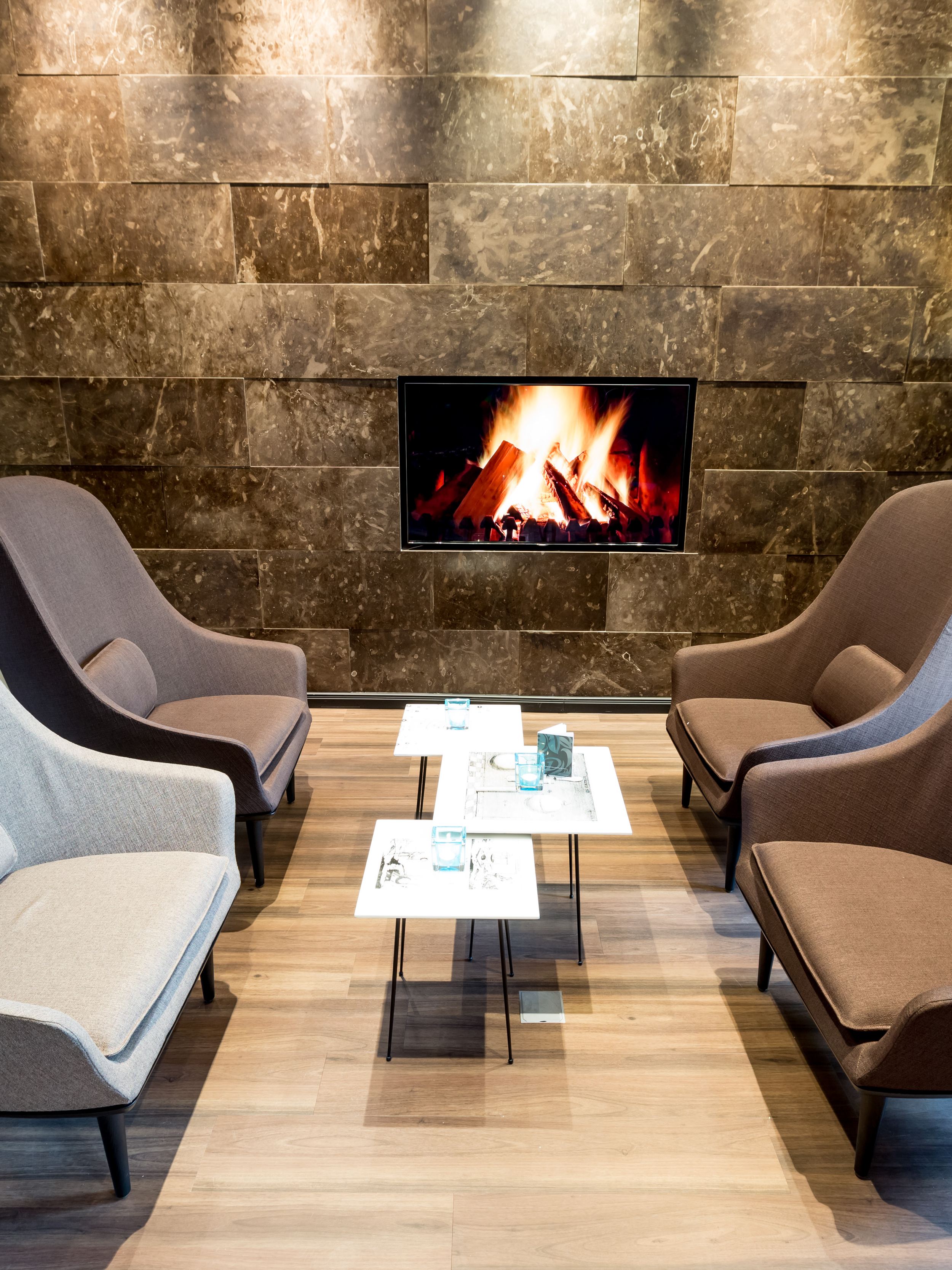 Designhotel Magdeburg Motel One Lounge vier Sessel mit Beistelltischen und Fernseher mit Feuer an der Wand