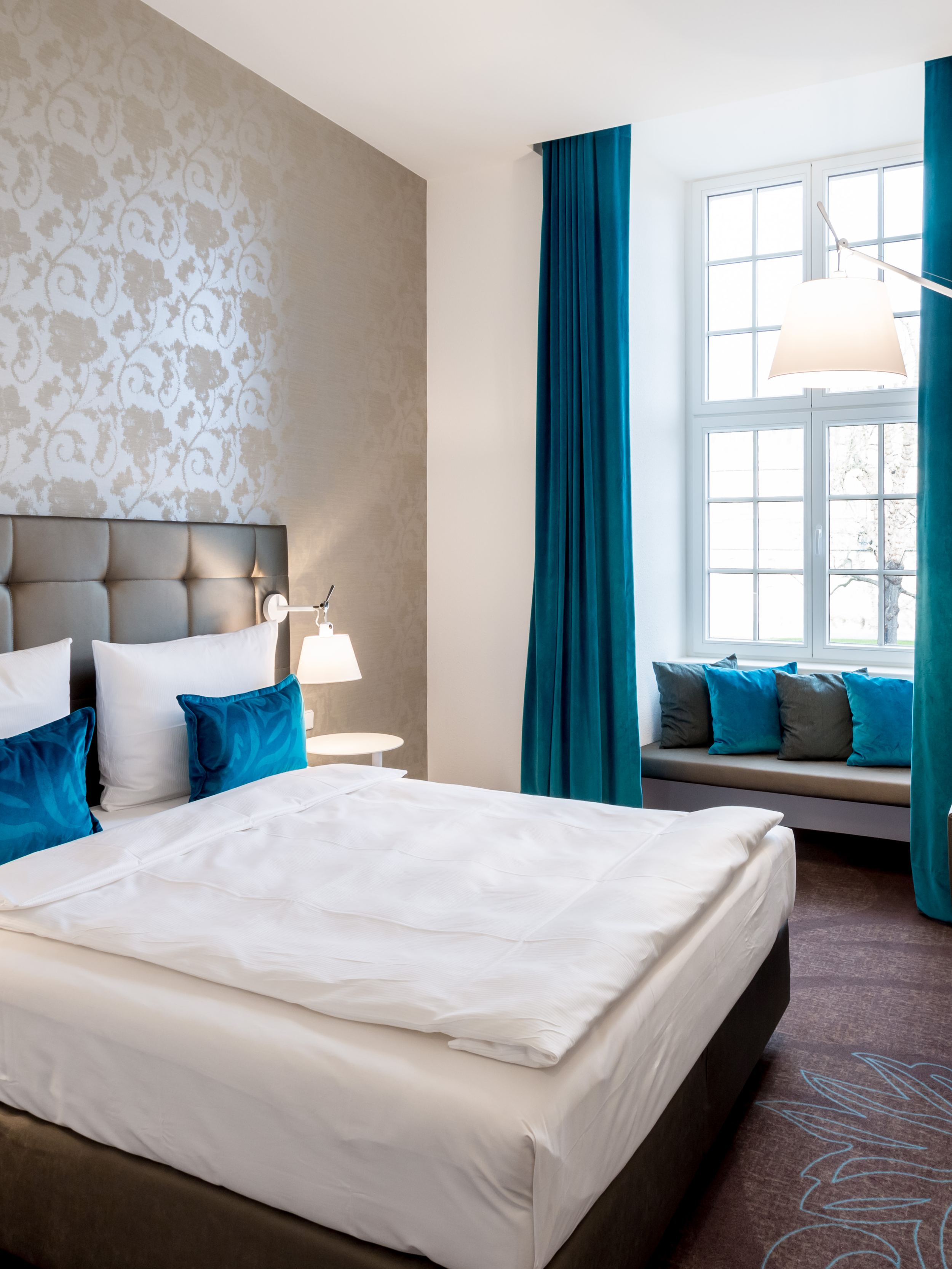 Hotel Magdeburg Motel One Schlafzimmer mit Doppelbett und einer Sitzbank vor dem großen Fenster