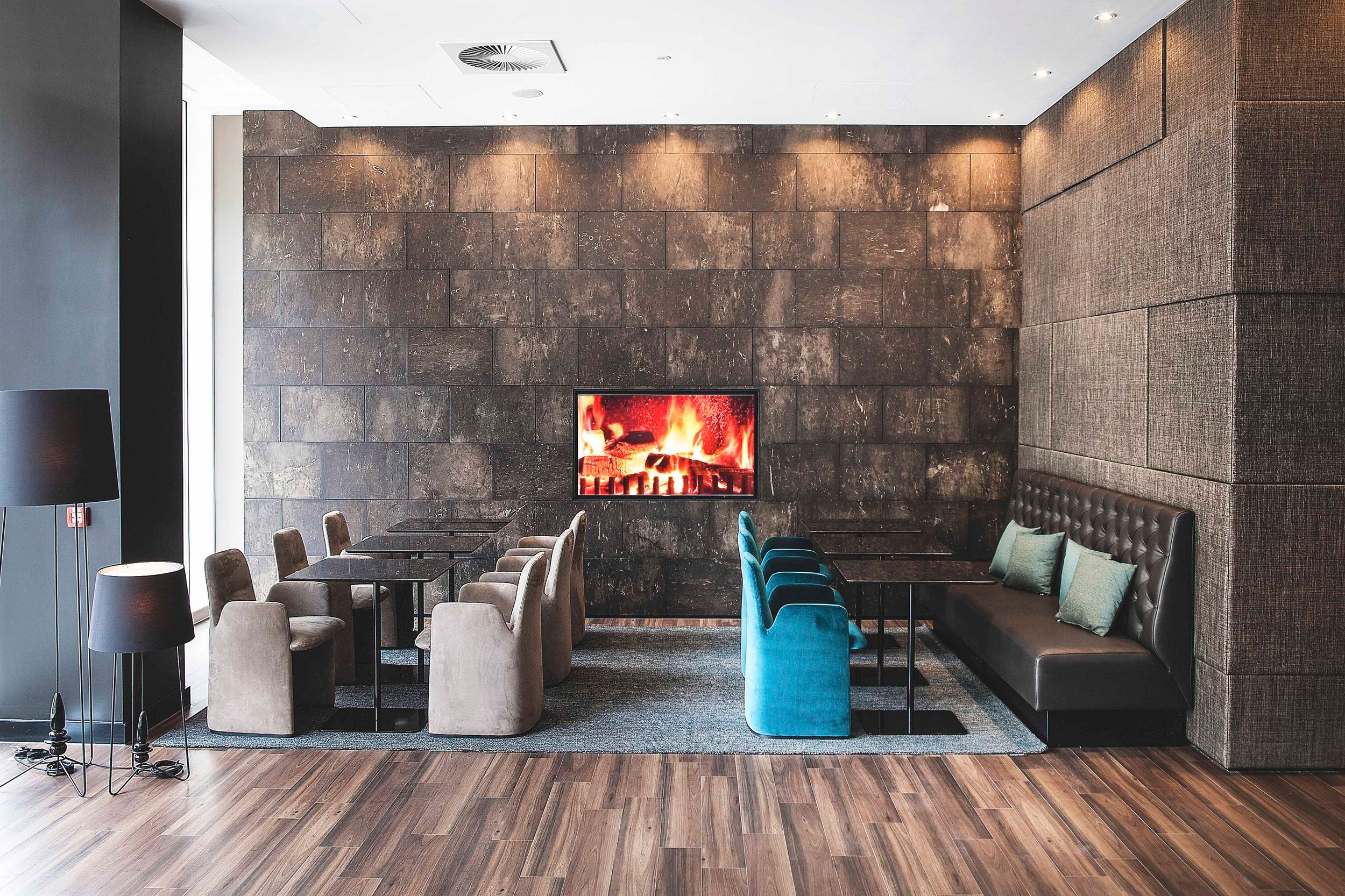 Hotel Manchester Piccadilly Motel One sechs Tische mit jeweils zwei Sitzplätzen und TV mit Feuerbild an der Wand