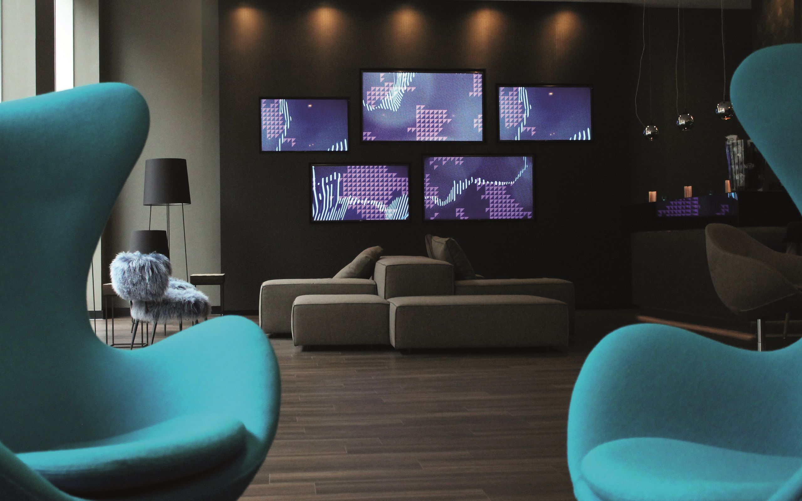 Hotel Manchester Piccadilly Motel One Lounge mit zwei Egg chairs im Vordergrund und Blick auf mehrere Fernseher an der Wand