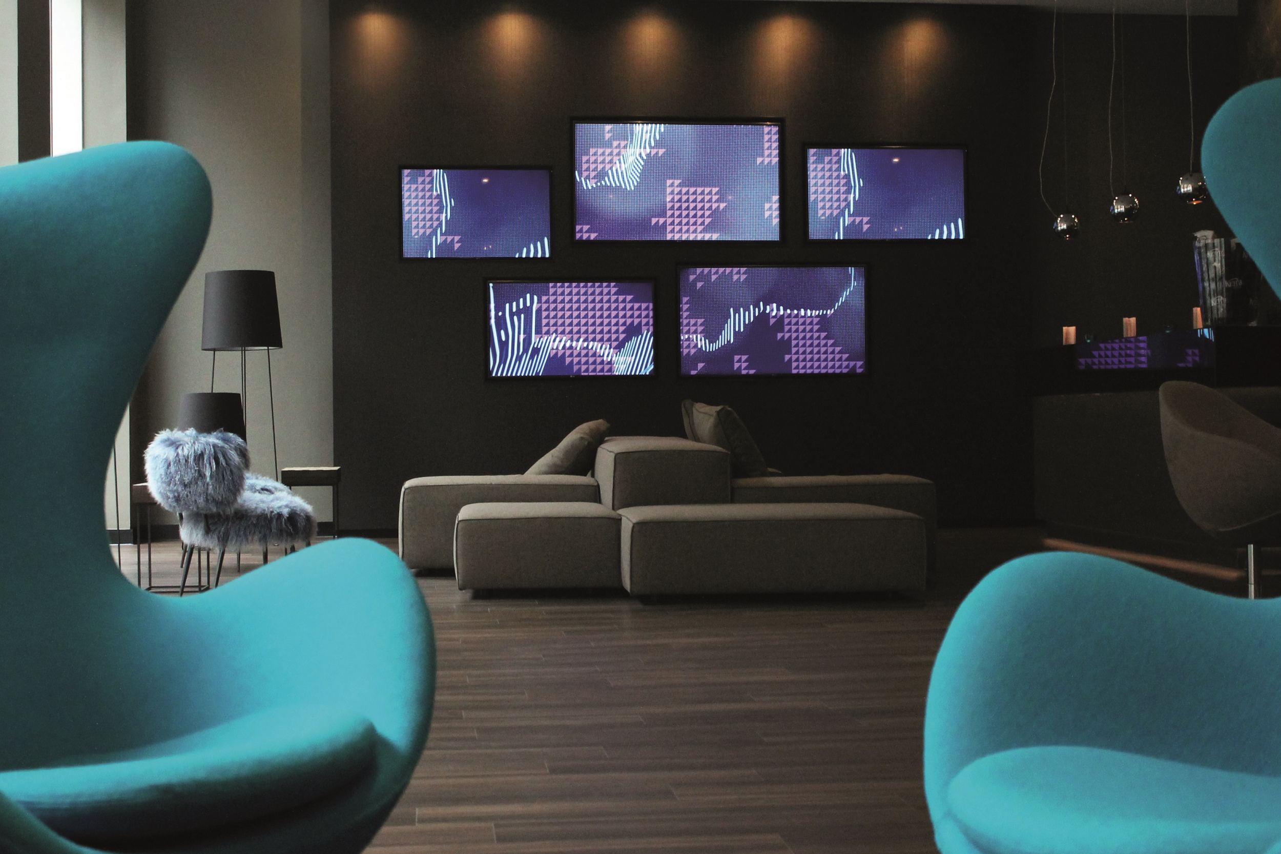 Hotel Manchester Piccadilly Motel One Lounge mit zwei Egg chairs im Vordergrund und Blick auf mehrere Fernseher an der Wand