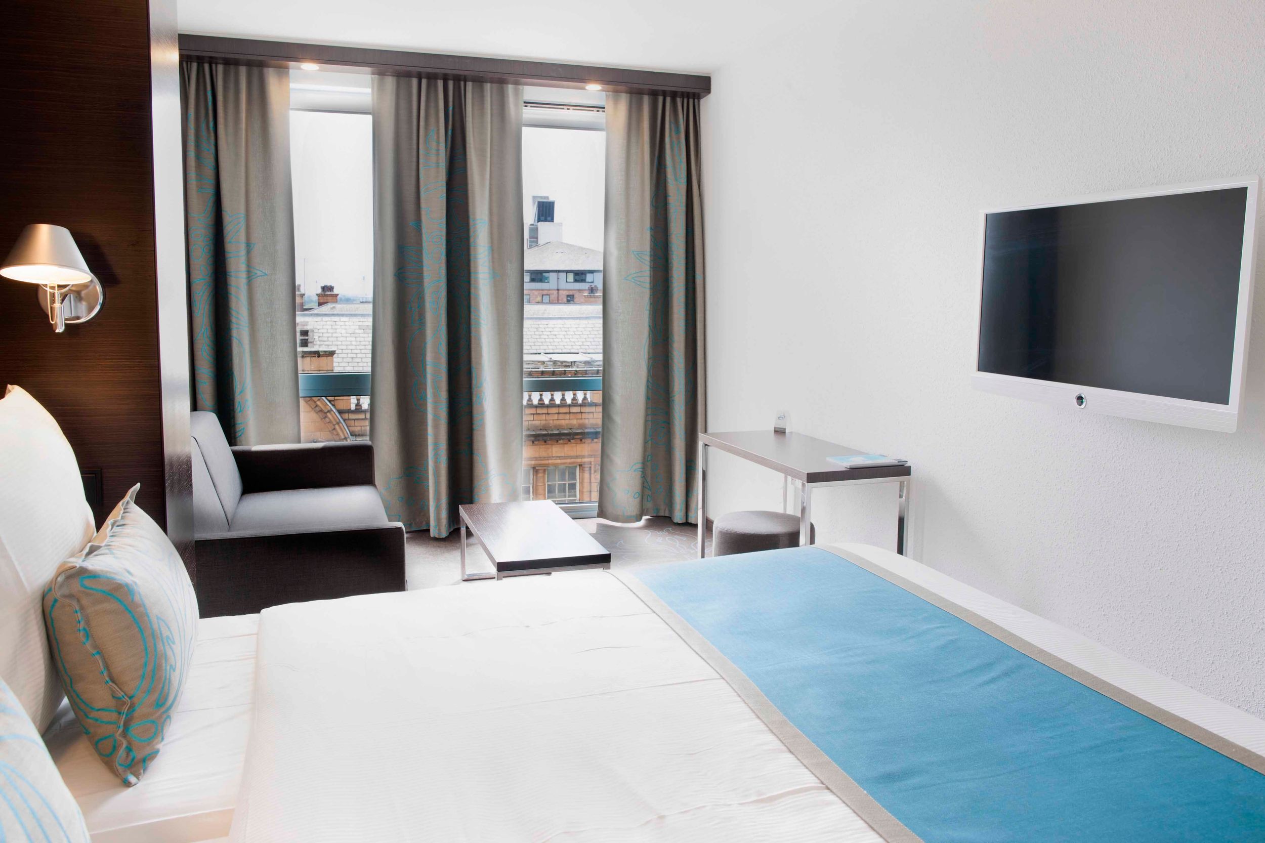 designhotel Manchester Piccadilly Motel One double bed, sofa in front of floor-to-ceiling window and TV on the wall