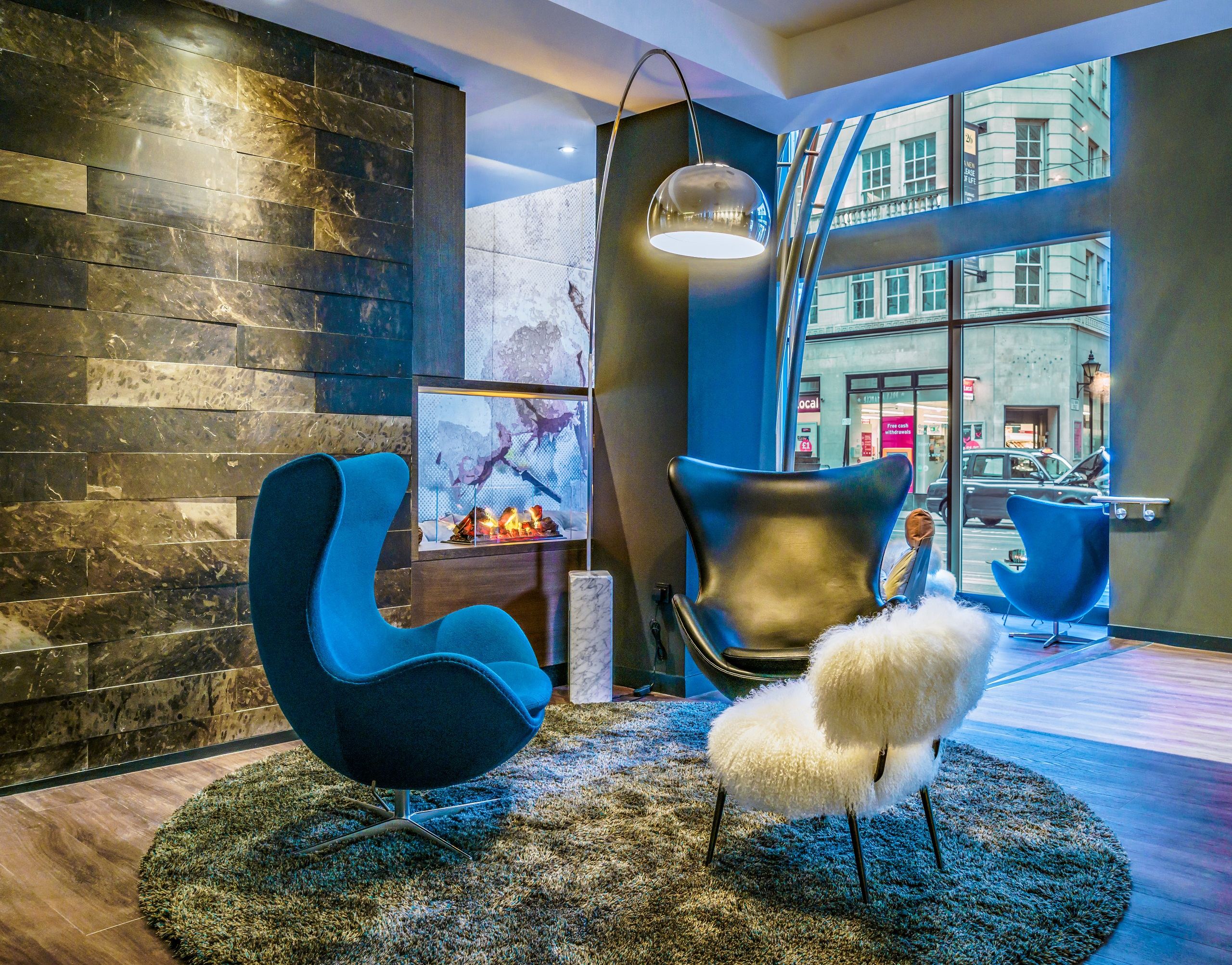 Hotel Manchester Royal Exchange Motel One zwei Egg chairs vor unechtem Kamin und großer Fensterfront Hotel Manchester Royal Exchange Motel One zwei Egg chairs vor unechtem Kamin und großer Fensterfront