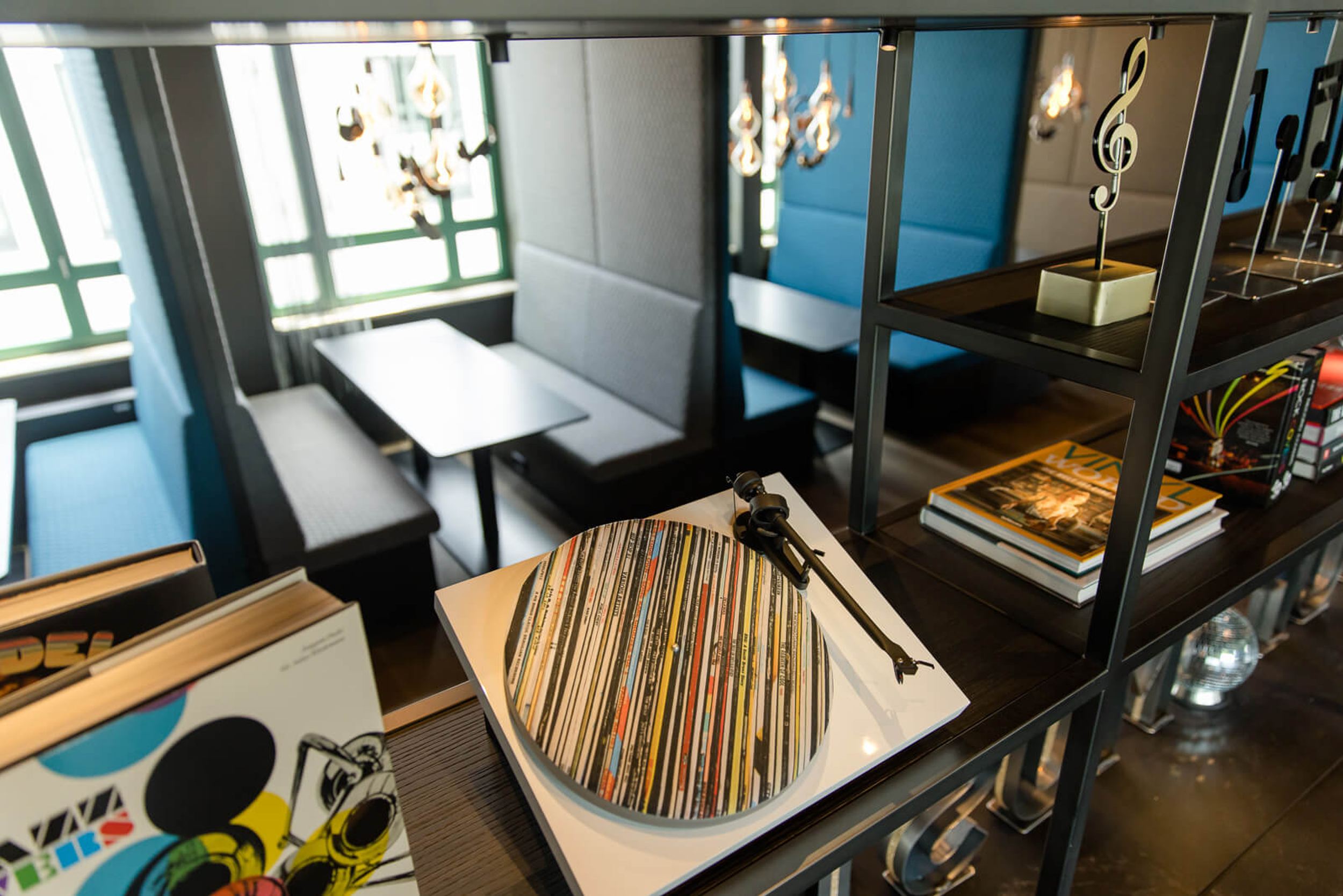 Hotel Mannheim Motel One Sitzgelegenheiten und offenes Regal mit Dekoration in Form eines Schallplattenspielers und Noten