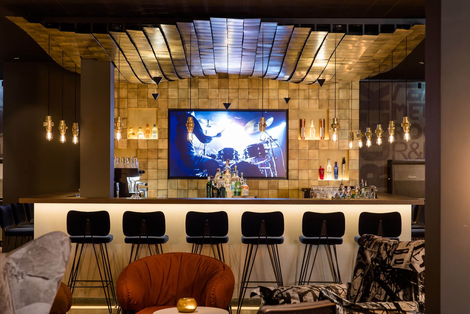 Hotel Mannheim Motel One Bar mit großem TV an der Wand sowie mehrere Barhocker und Sessel