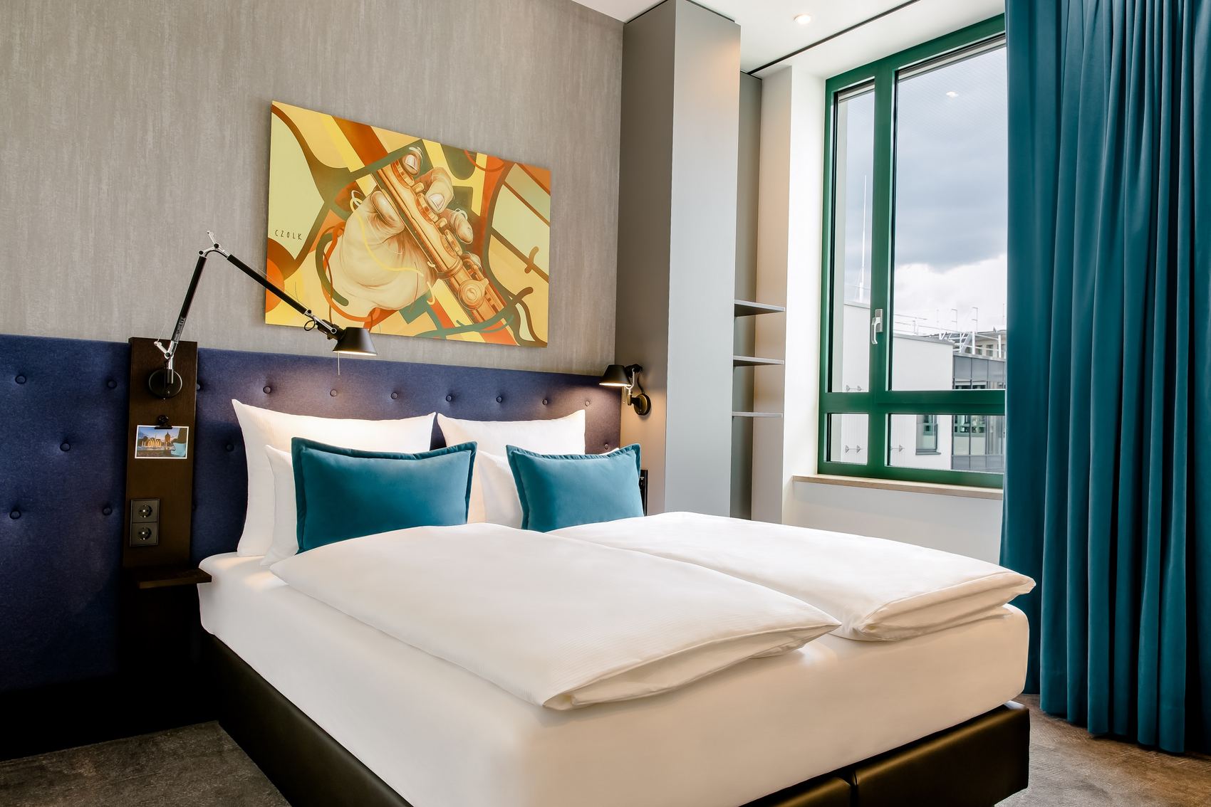Hotel Mannheim Motel One helles Zimmer mit komfortablem Doppelbett und gelbem Bild mit Querflöte an der Wand