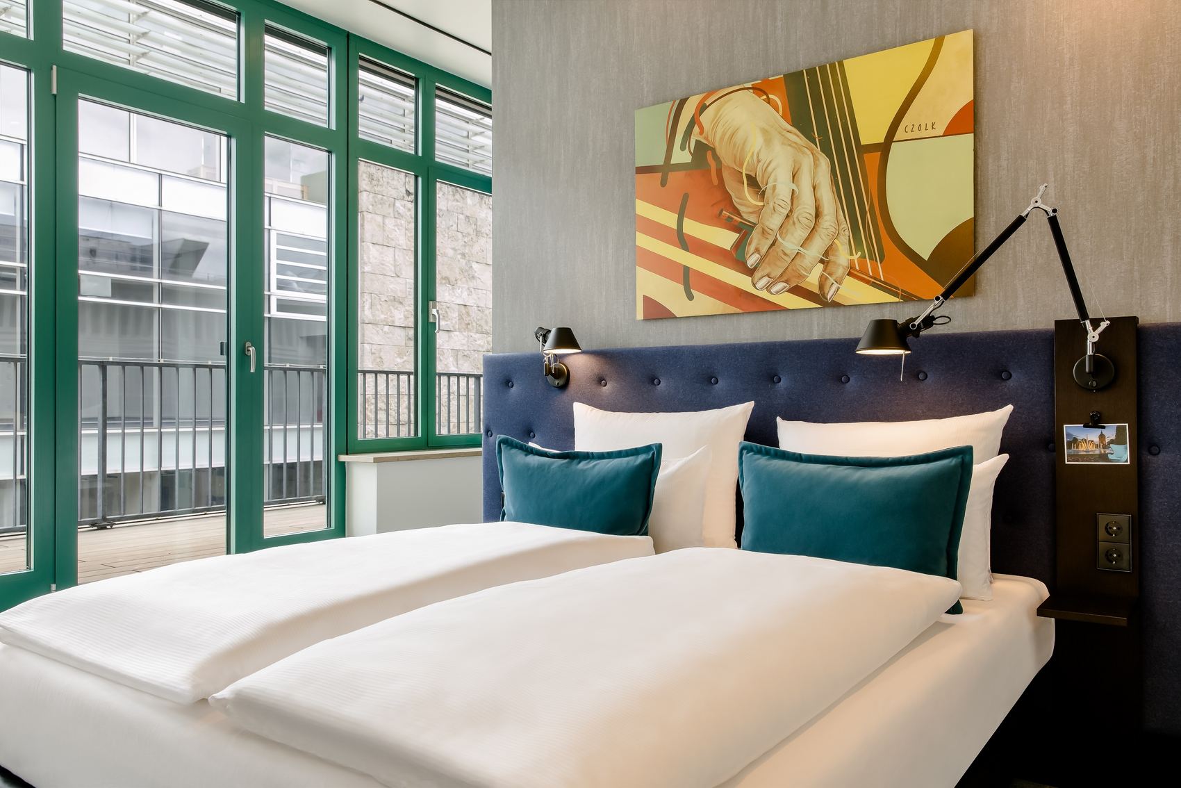 Hotel Mannheim Motel One Blick auf großes Doppelbett sowie Fensterfront mit Balkon