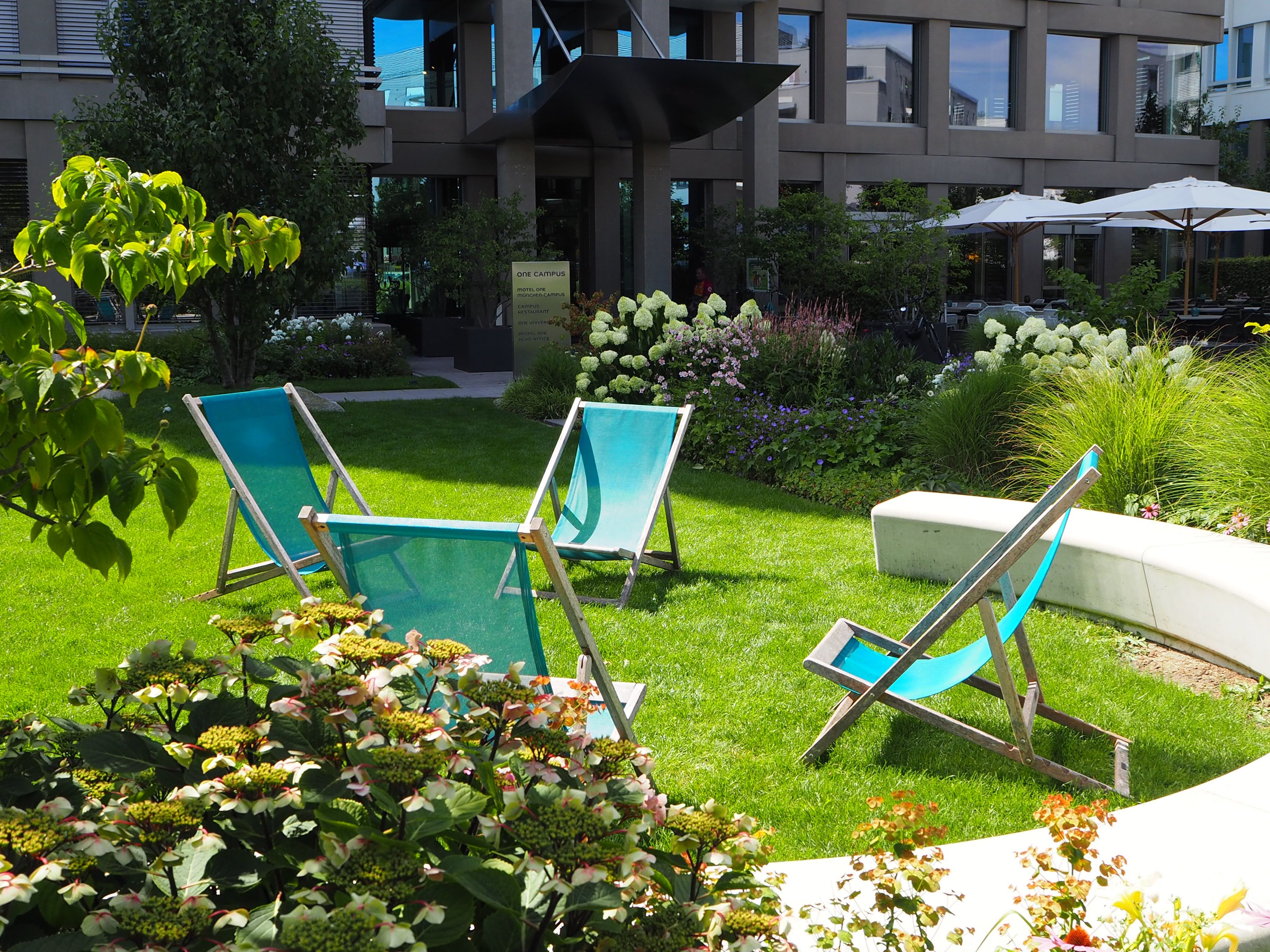 Hotel München Campus Motel One Außenbereich Liegestühle auf der Wiese