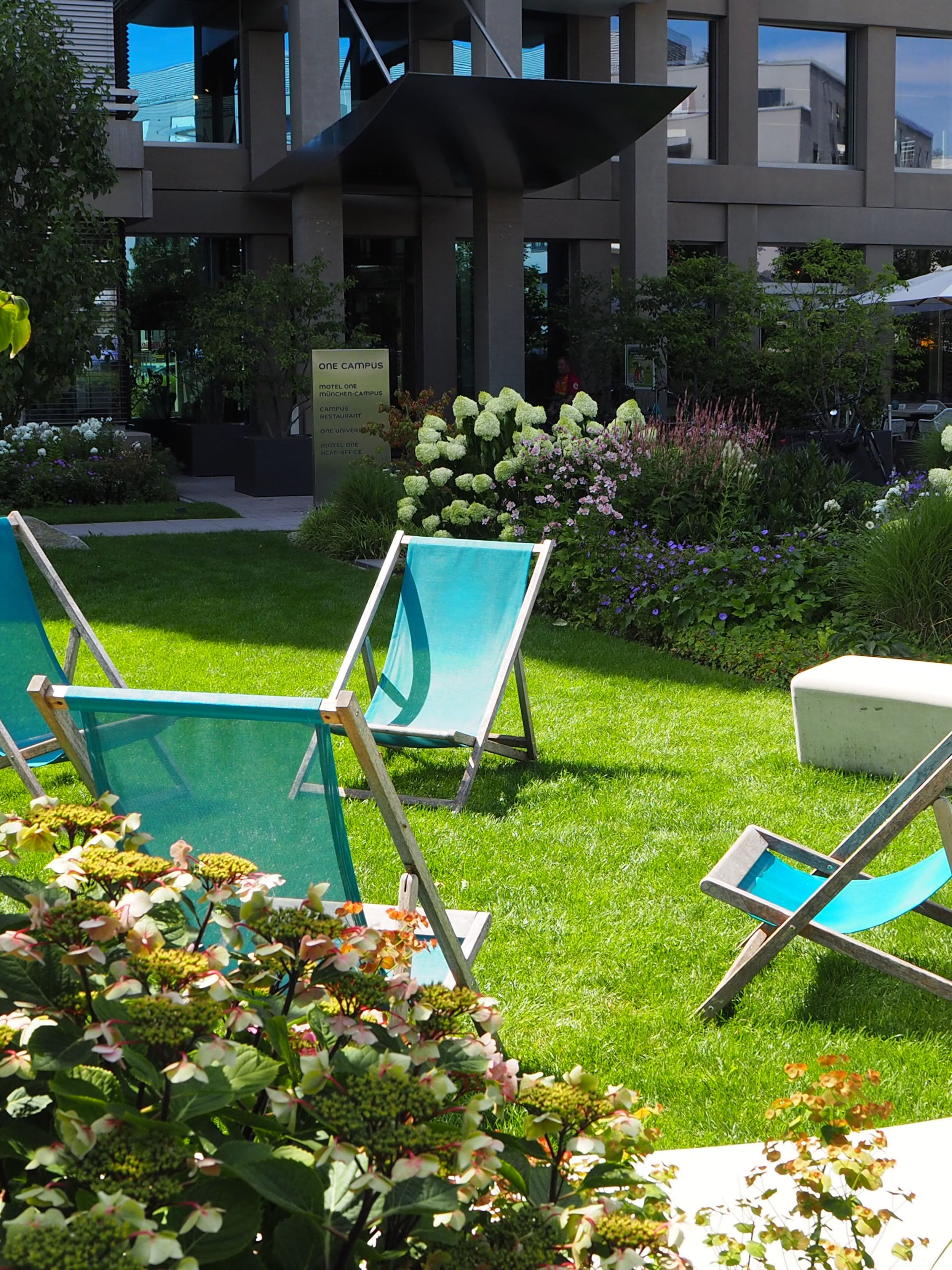 Hotel München Campus Motel One Außenbereich Liegestühle auf der Wiese