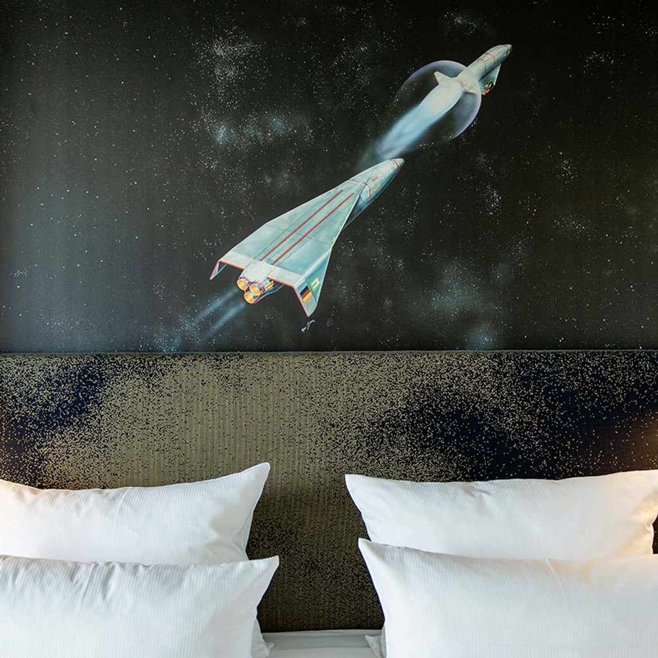 Designhotel Deutsches Museum Motel One Blick auf Kopfteil eines Doppelbettes sowie Wandbild mit zwei Raketen