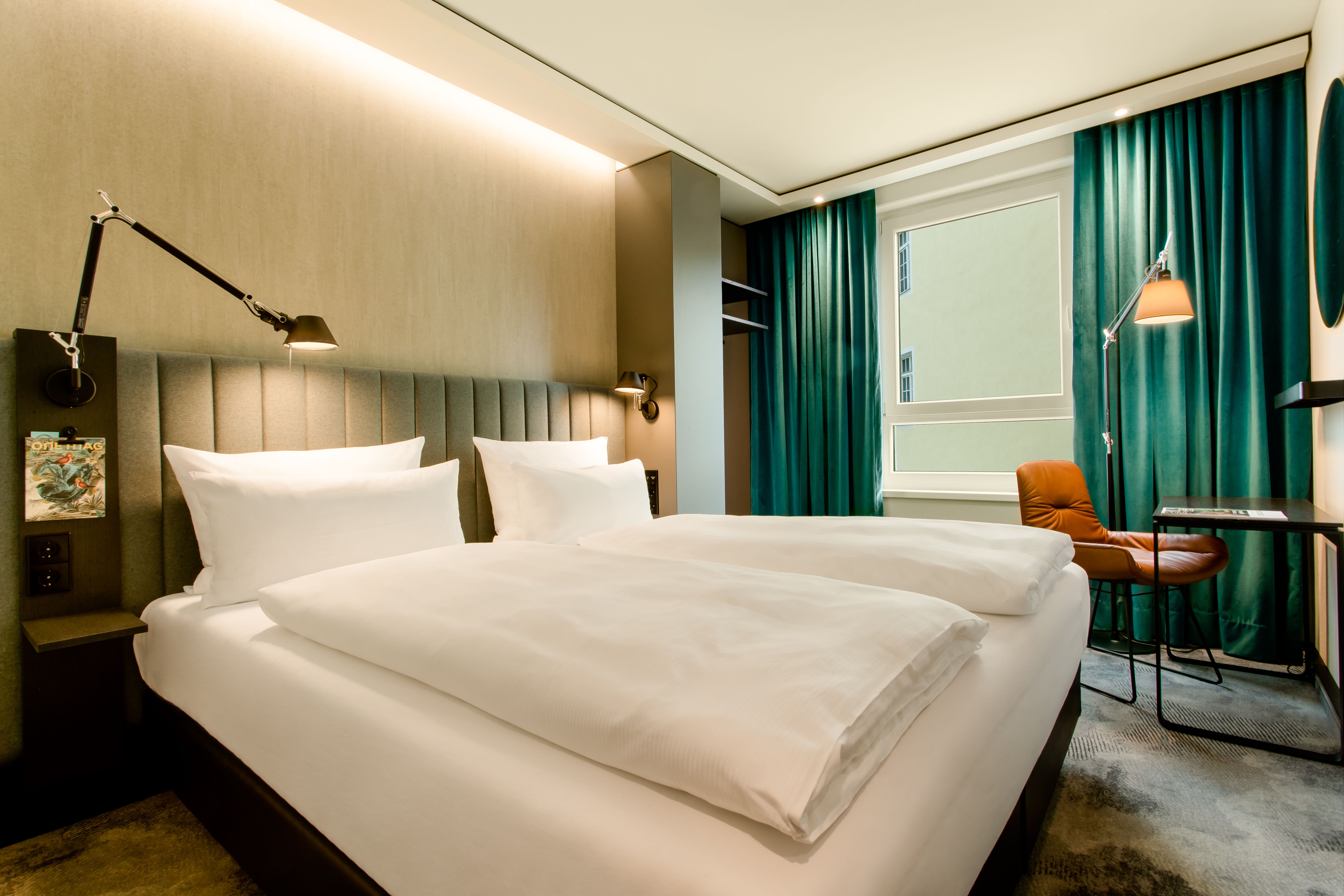 Designhotel East Side Motel One seitlicher Blick in helles Doppelzimmer mit Tisch und Sessel