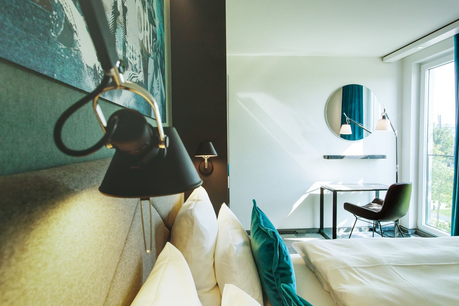 Designhotel Garching Motel One seitlicher Blick über Doppelbett auf Schreibtisch, Stuhl und Spiegel