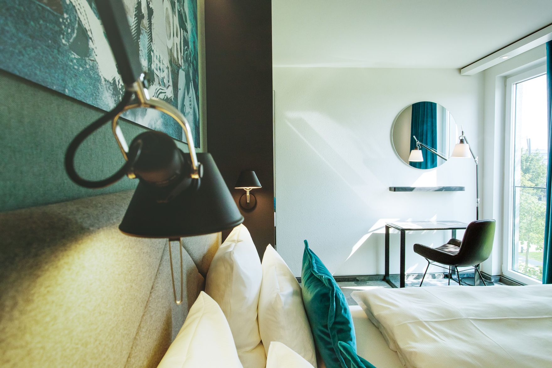 Designhotel Garching Motel One seitlicher Blick über Doppelbett auf Schreibtisch, Stuhl und Spiegel
