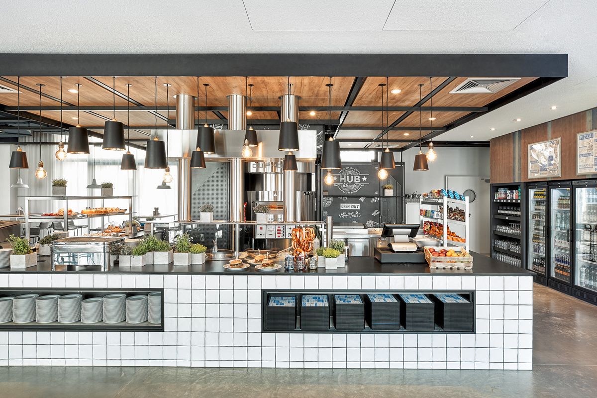 Moderne Hotelküche mit offenem Buffet, frischen Backwaren, Obst und Getränken. Helle, einladende Atmosphäre mit klarer Struktur, ideal für ein entspanntes Frühstück oder einen schnellen Snack. Elegantes Design mit warmen Holzakzenten und funktionaler Beleuchtung.