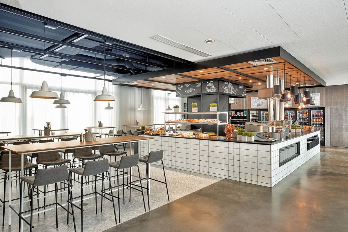 Modernes, helles Buffet-Restaurant mit großer Theke, verschiedenen Speisen und Getränken sowie mehreren Sitzbereichen, ideal für entspanntes Frühstück oder Mittagessen in angenehmer Atmosphäre.
