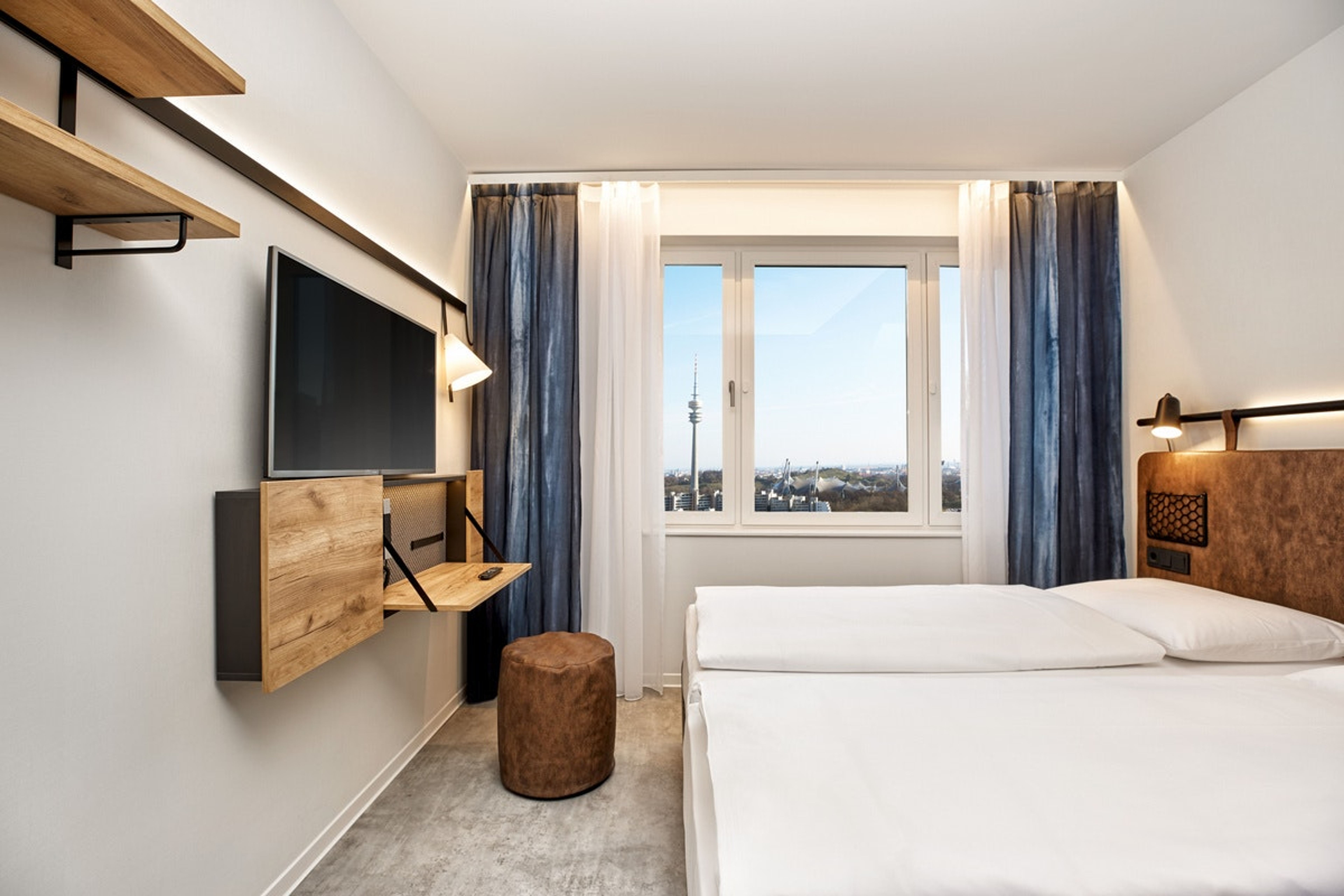 Helles, modernes Hotelzimmer mit zwei Einzelbetten, großem Fenster und Blick auf eine Stadt mit Fernsehturm. Minimalistische Einrichtung mit Wand-TV, Holzregalen und komfortablem Sitzhocker. Angenehme Atmosphäre für Geschäfts- und Urlaubsreisende. Helles, modernes Hotelzimmer mit zwei Einzelbetten, großem Fenster und Blick auf eine Stadt mit Fernsehturm. Minimalistische Einrichtung mit Wand-TV, Holzregalen und komfortablem Sitzhocker. Angenehme Atmosphäre für Geschäfts- und Urlaubsreisende.