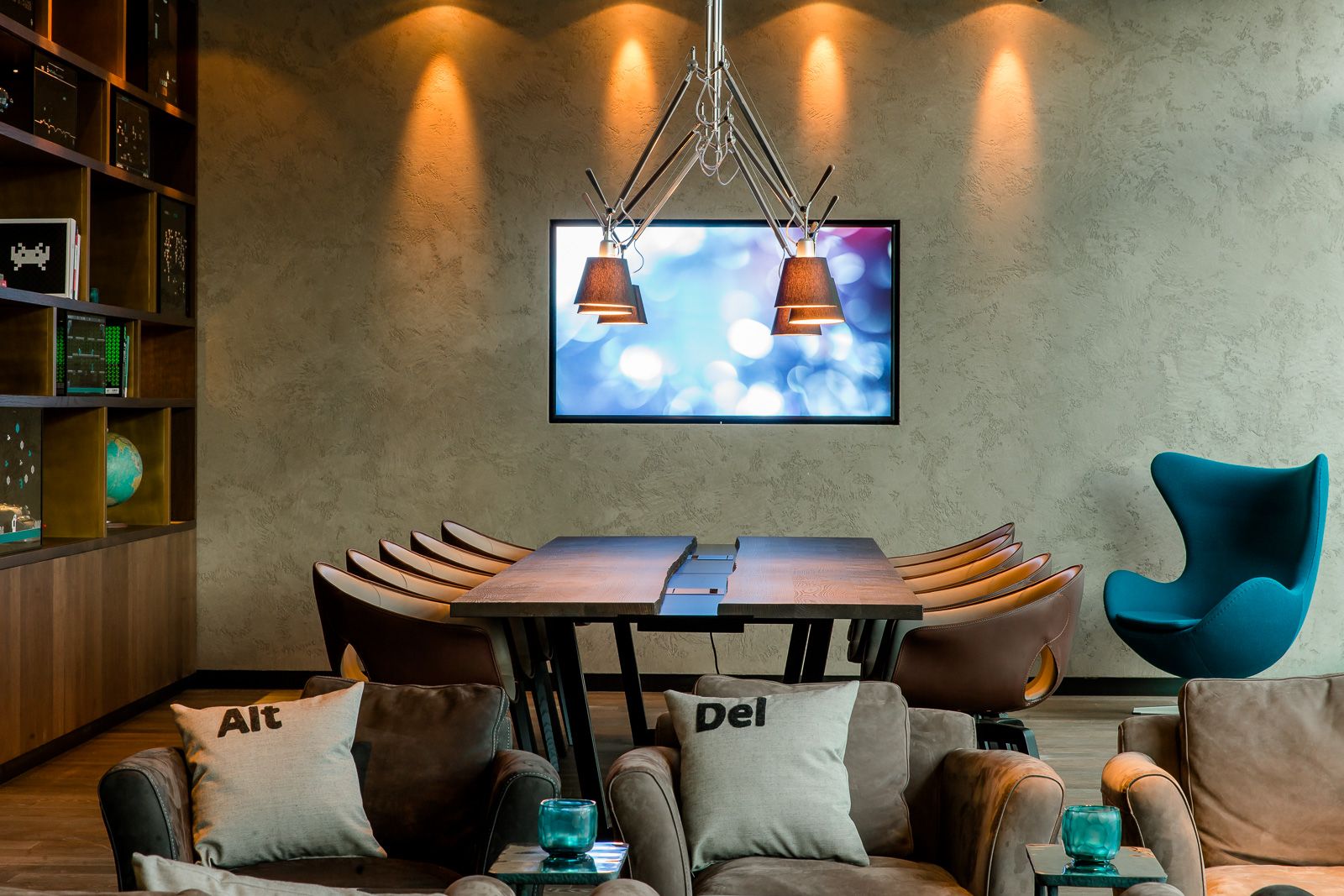 Hotel München Parkstadt Schwabing Motel One Meetingraum mit Tisch und Stühlen sowie TV an der Wand und Sessel im Vordergrund