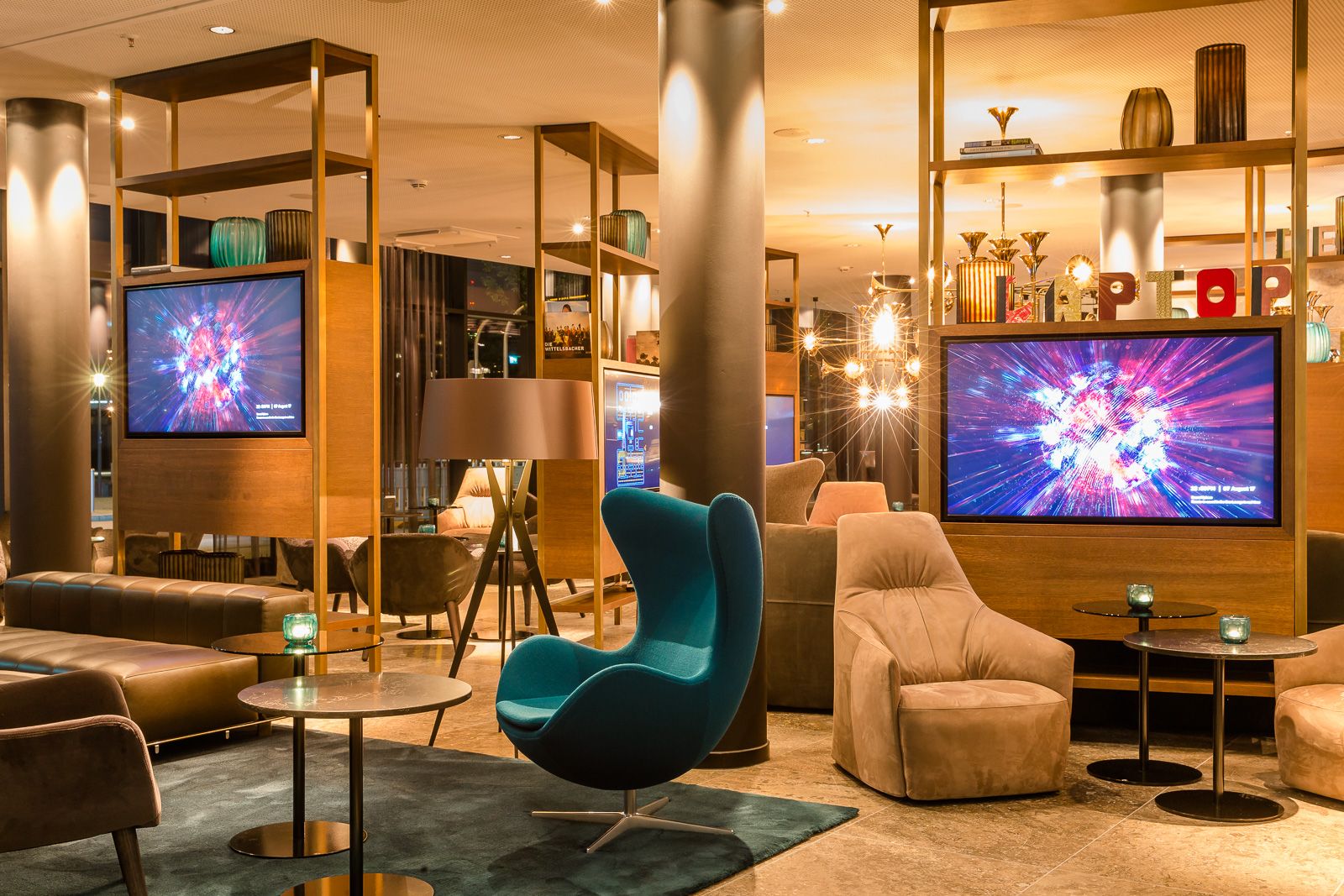 Designhotel München Parkstadt Schwabing Motel One Lounge am Abend mit Sesseln, Egg Chair und zwei Fernsehern