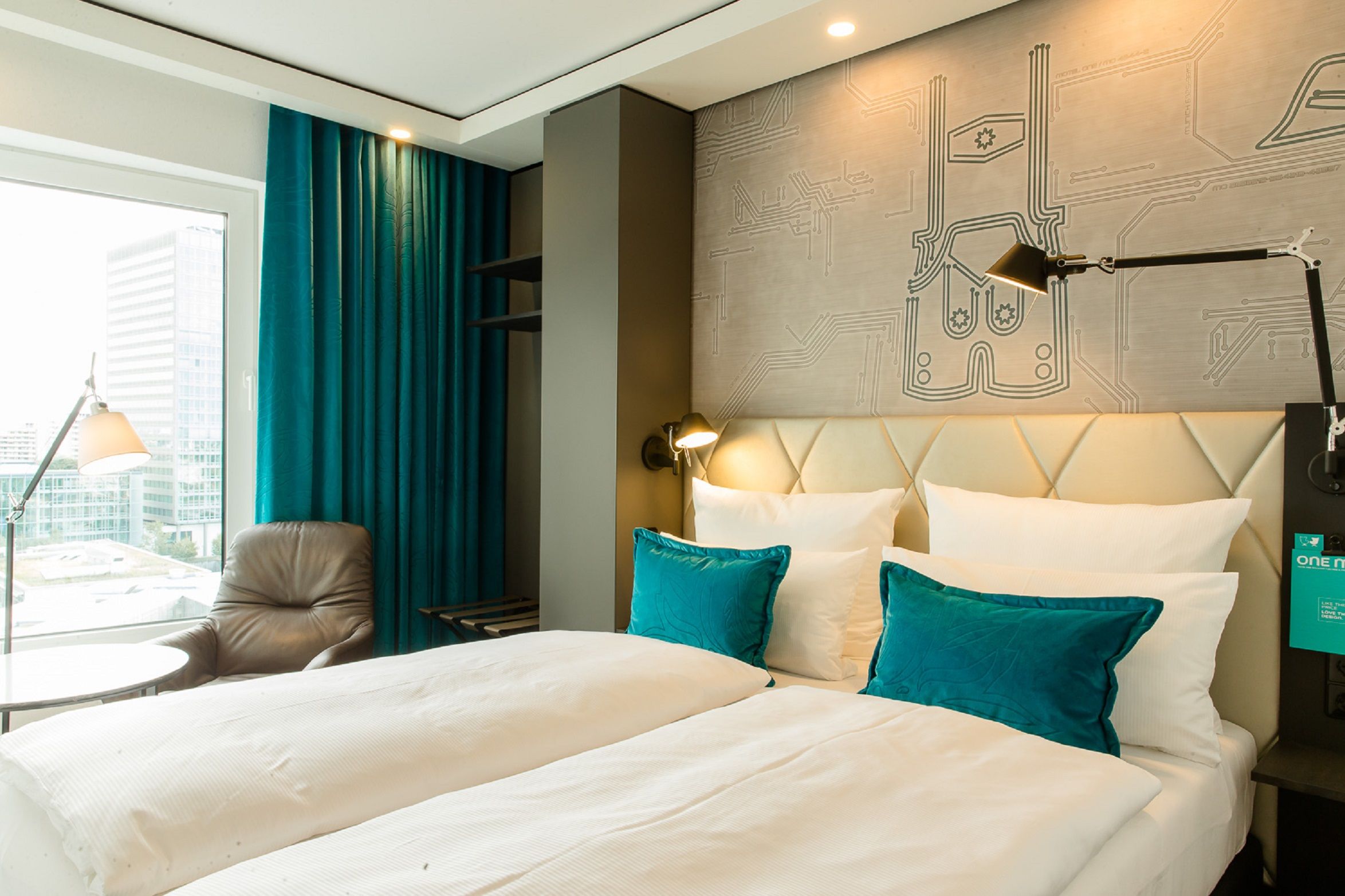Designhotel München Parkstadt Schwabing Motel One seitlicher Blick in helles Hotelzimmer mit großem Doppelbett