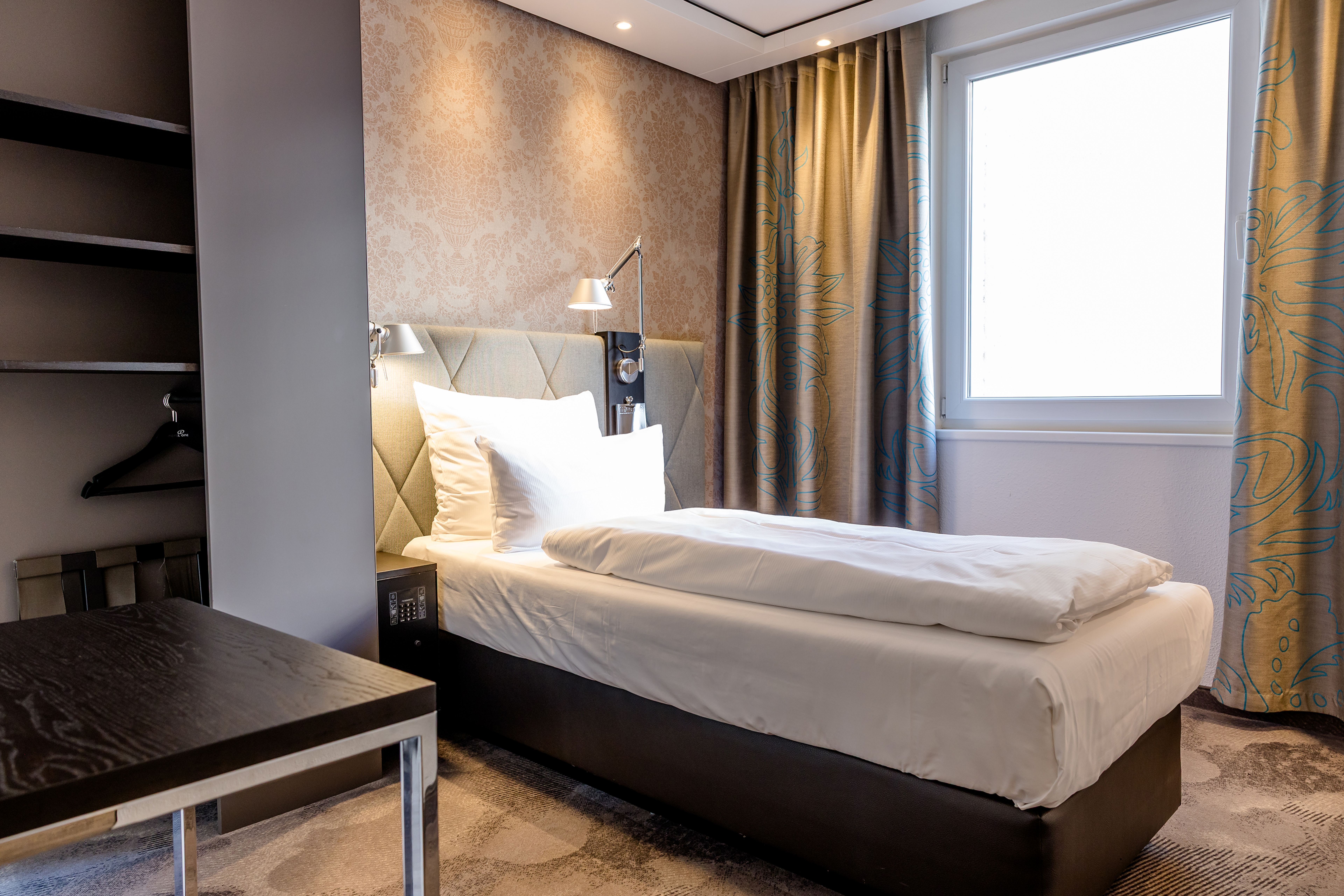 Hotel Motel One München-Sendlinger Tor Helles Einzelzimmer mit modernem Design, komfortablem Bett, weichen Kissen, Leselampen und einem Fenster mit Blick nach draußen. Vorhänge und dezente Wandgestaltung erzeugen eine gemütliche Atmosphäre. Hotel Motel One München-Sendlinger Tor Helles Einzelzimmer mit modernem Design, komfortablem Bett, weichen Kissen, Leselampen und einem Fenster mit Blick nach draußen. Vorhänge und dezente Wandgestaltung erzeugen eine gemütliche Atmosphäre.