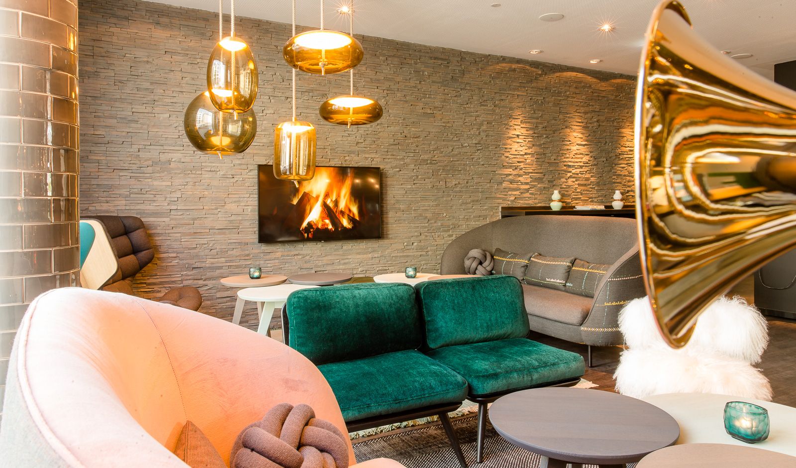 Hotel München Westend Motel One helle Lounge mit Couches und Sesseln sowie Fernseher mit Feuer an der Wand