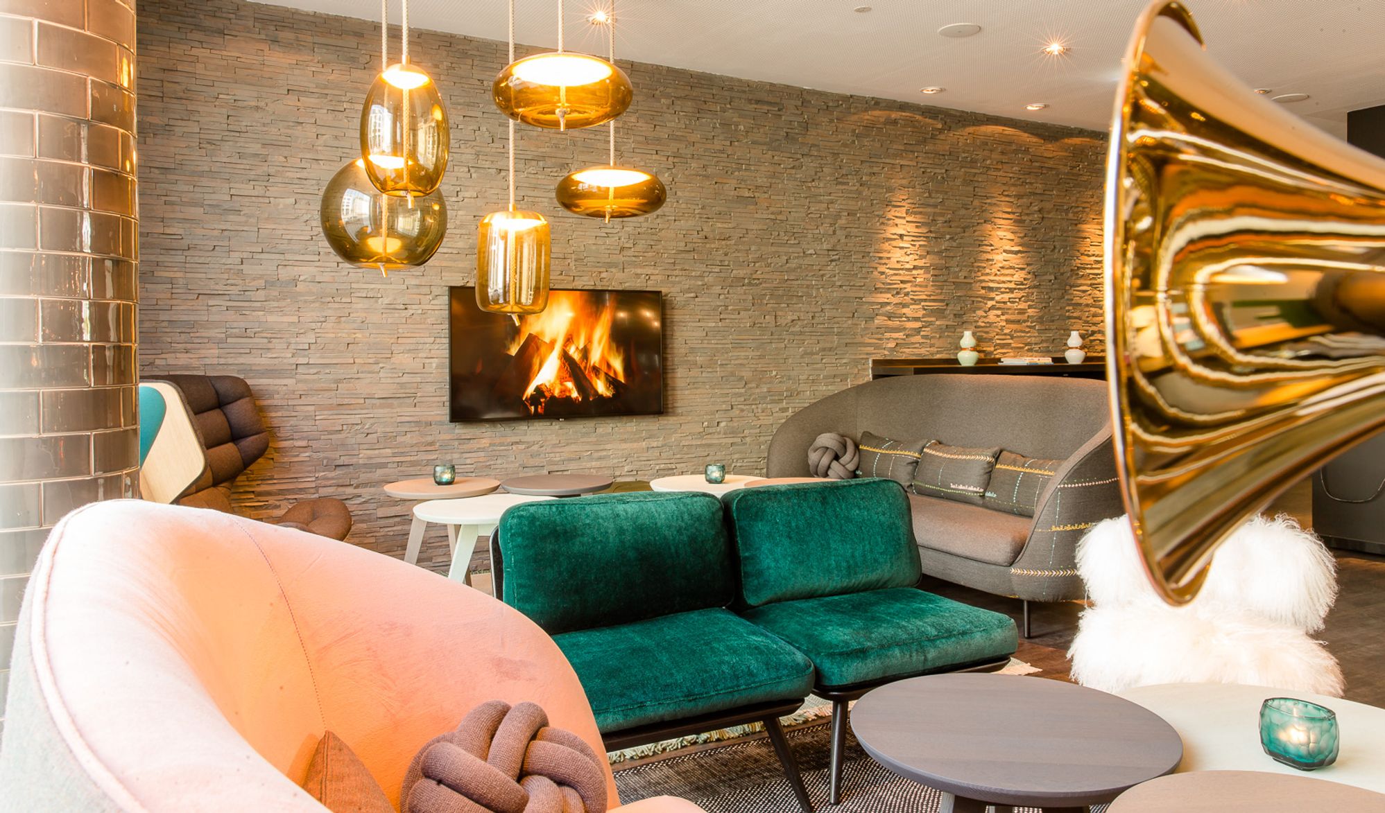 Hotel München Westend Motel One helle Lounge mit Couches und Sesseln sowie Fernseher mit Feuer an der Wand