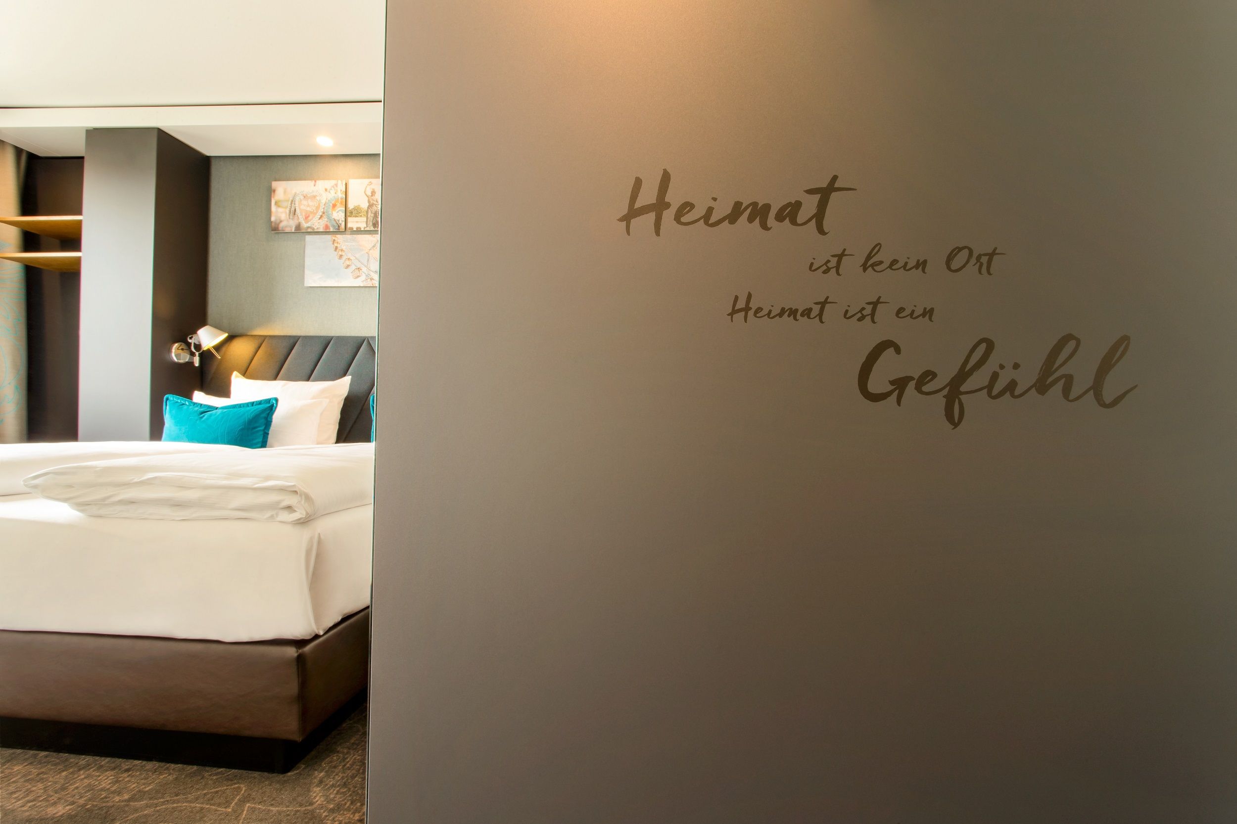 Designhotel München Westend Motel One Zimmer mit Doppelbett und Schriftzug "Heimat ist kein Ort, Heimat ist ein Gefühl" an der Wand