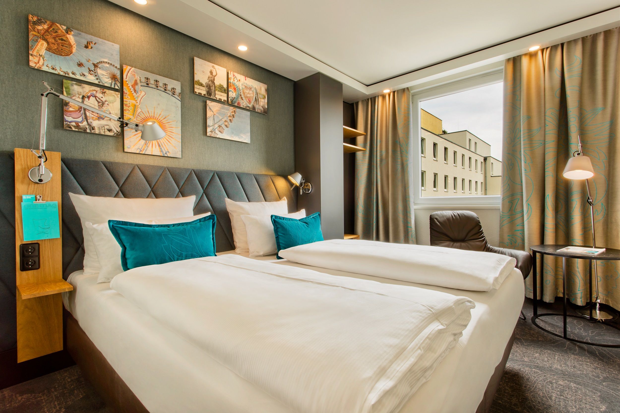 Designhotel München Westend Motel One seitlicher Blick in helles Zimmer mit Doppelbett, Sessel und rundem Beistelltisch