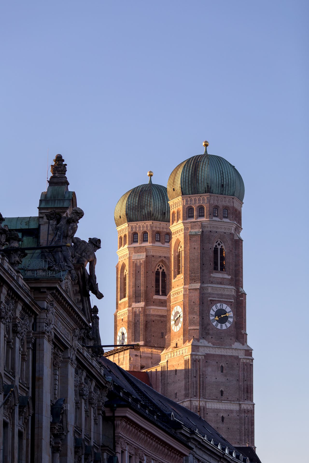 Die beiden markanten Zwiebeltürme der Frauenkirche in München leuchten im warmen Abendlicht vor klarem Himmel.