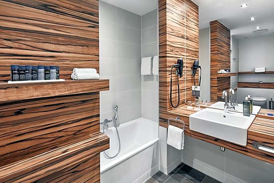 Modernes Badezimmers mit Badewanne, großem Spiegel und Waschbecken. Holzvertäfelungen schaffen warme Atmosphäre. Handtücher und Pflegeprodukte sind bereitgestellt für Komfort und Entspannung.
