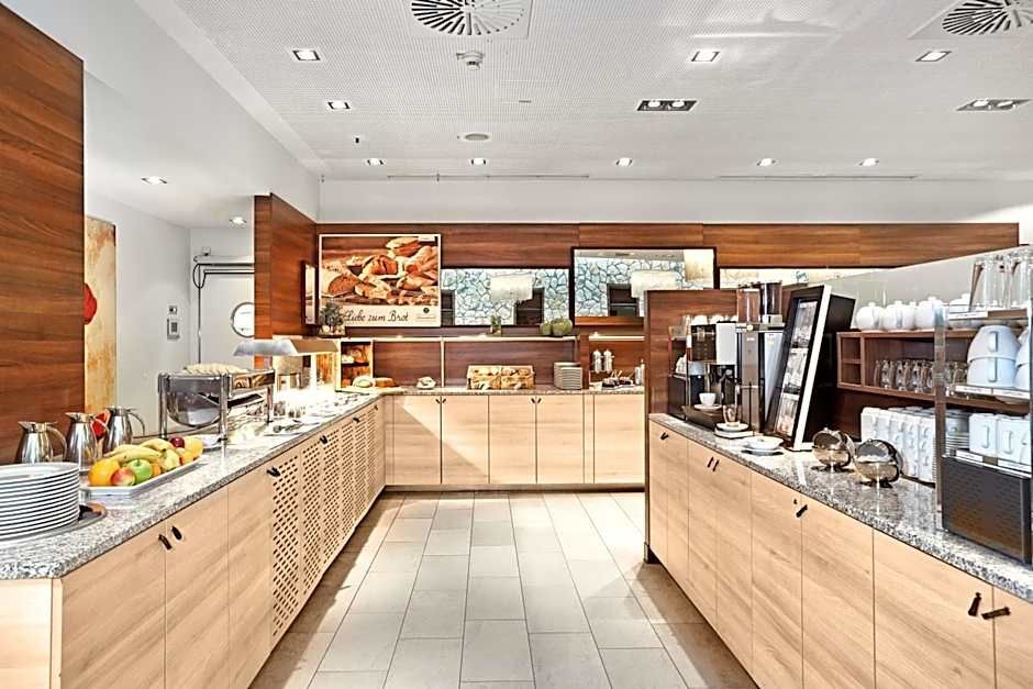 Helles, modernes Frühstücksbuffet mit Müsli, frischem Obst, Kaffee- und Saftautomaten in stilvollem Holz- und Marmorambiente, ideal für einen gelungenen Start in den Tag.