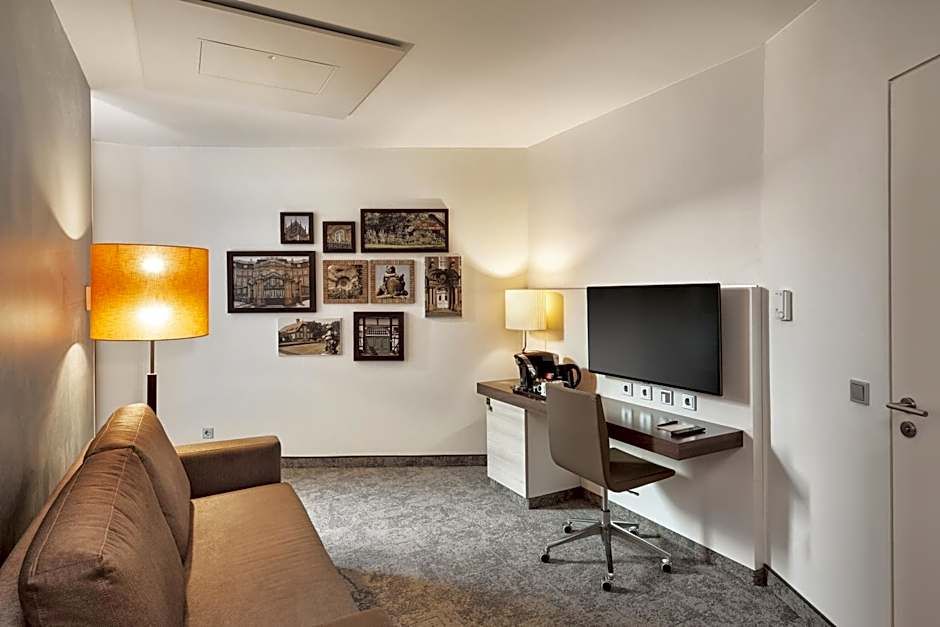 Gemütlicher Hotelzimmerbereich mit Couch, Arbeitsbereich, Wandbildern und warmem Licht, ideal für entspannte Abende oder produktives Arbeiten.