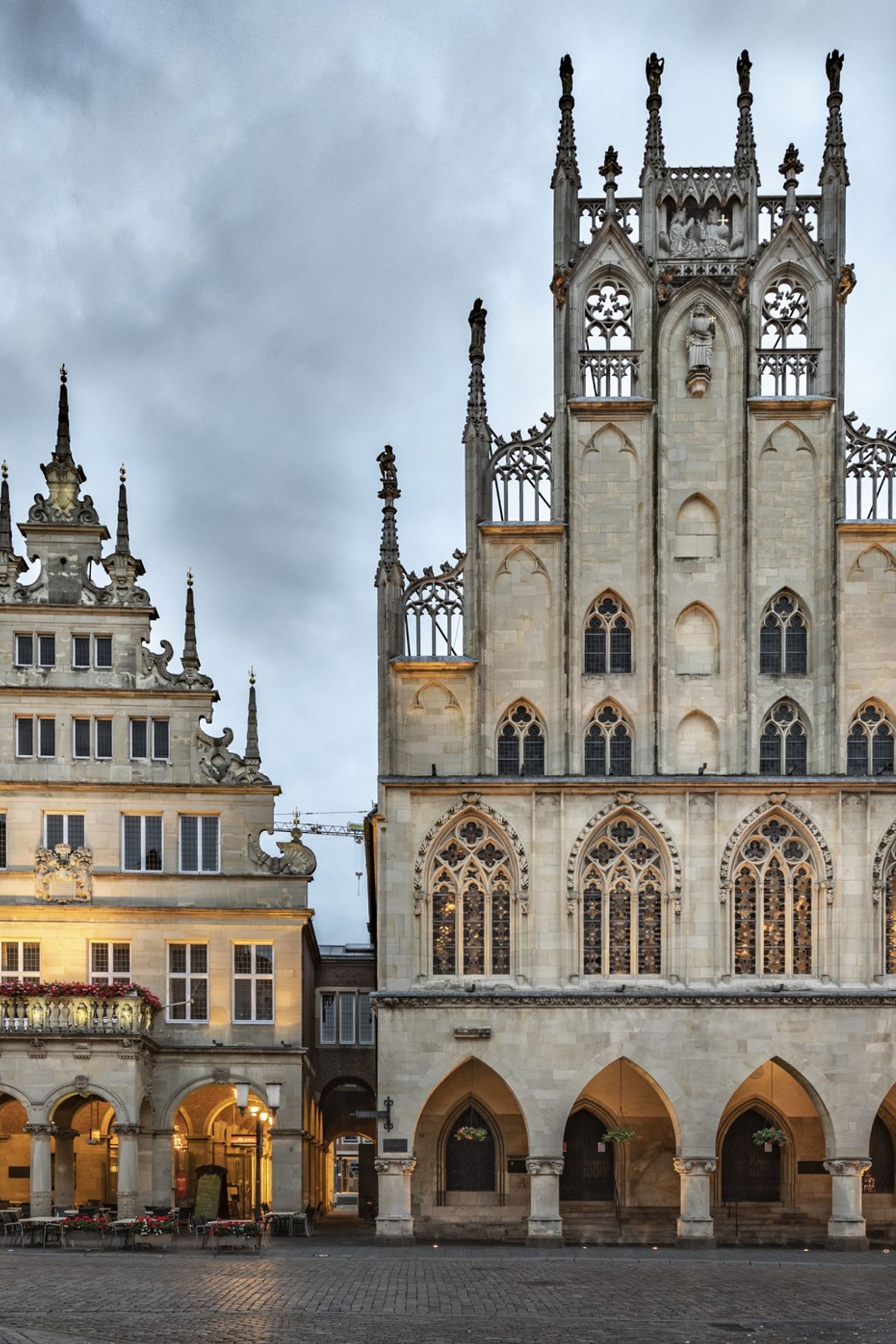 Blick auf das historische Rathaus mit gotischer Fassade und dem angrenzenden Renaissance-Gebäude am belebten Marktplatz, umgeben von weiteren historischen Gebäuden unter bewölktem Himmel.
