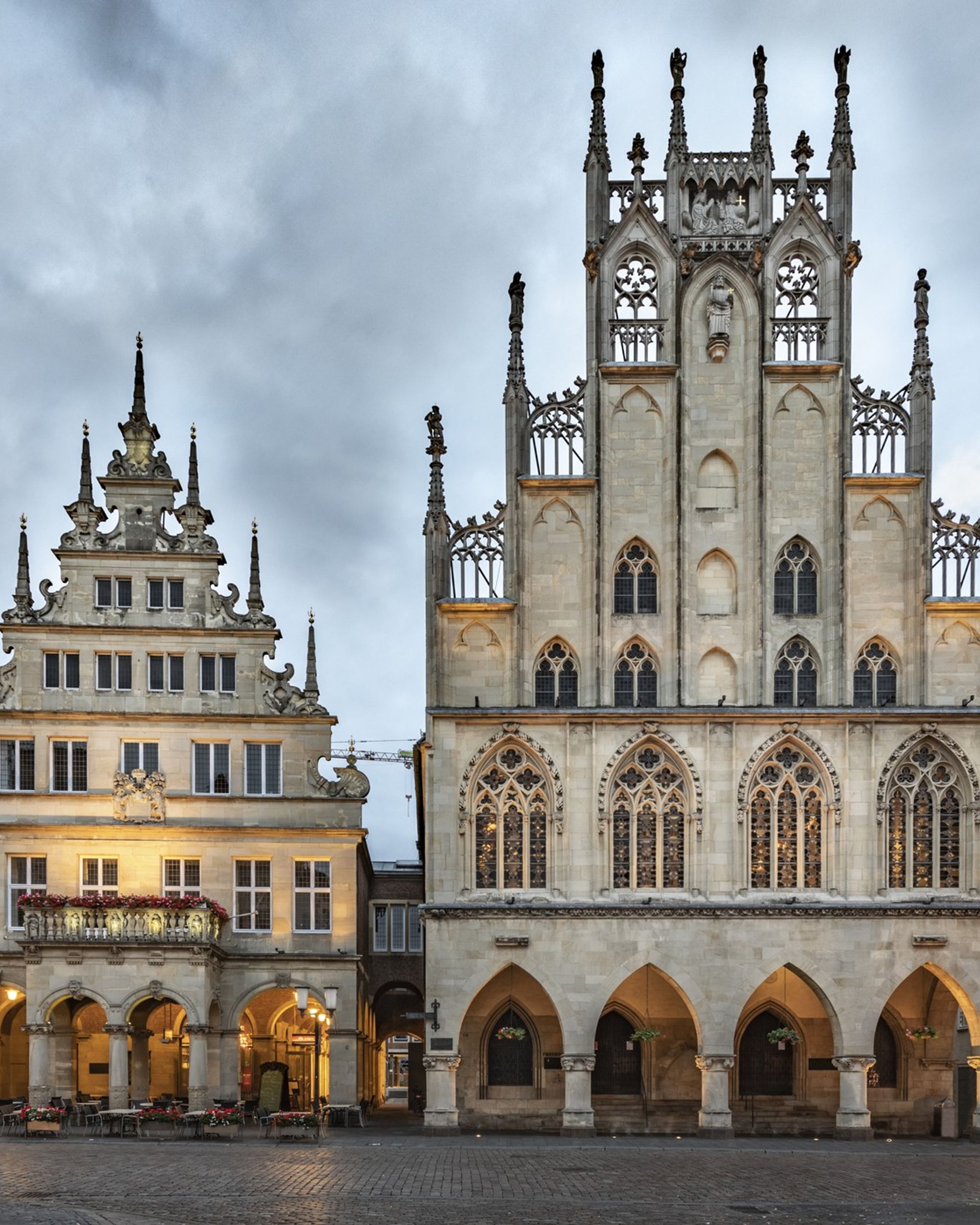 Blick auf das historische Rathaus mit gotischer Fassade und dem angrenzenden Renaissance-Gebäude am belebten Marktplatz, umgeben von weiteren historischen Gebäuden unter bewölktem Himmel.