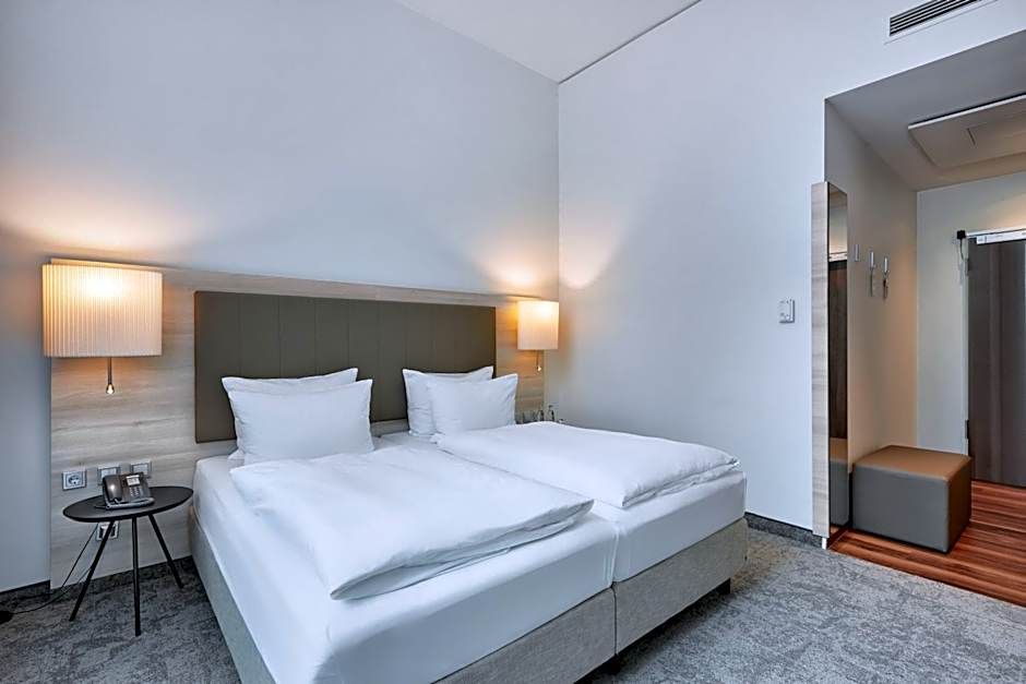 Helles, modernes Hotelzimmer mit zwei getrennten Einzelbetten, weissen Bettwäsche, Nachttischlampen und schlichtem, gemütlichem Ambiente.