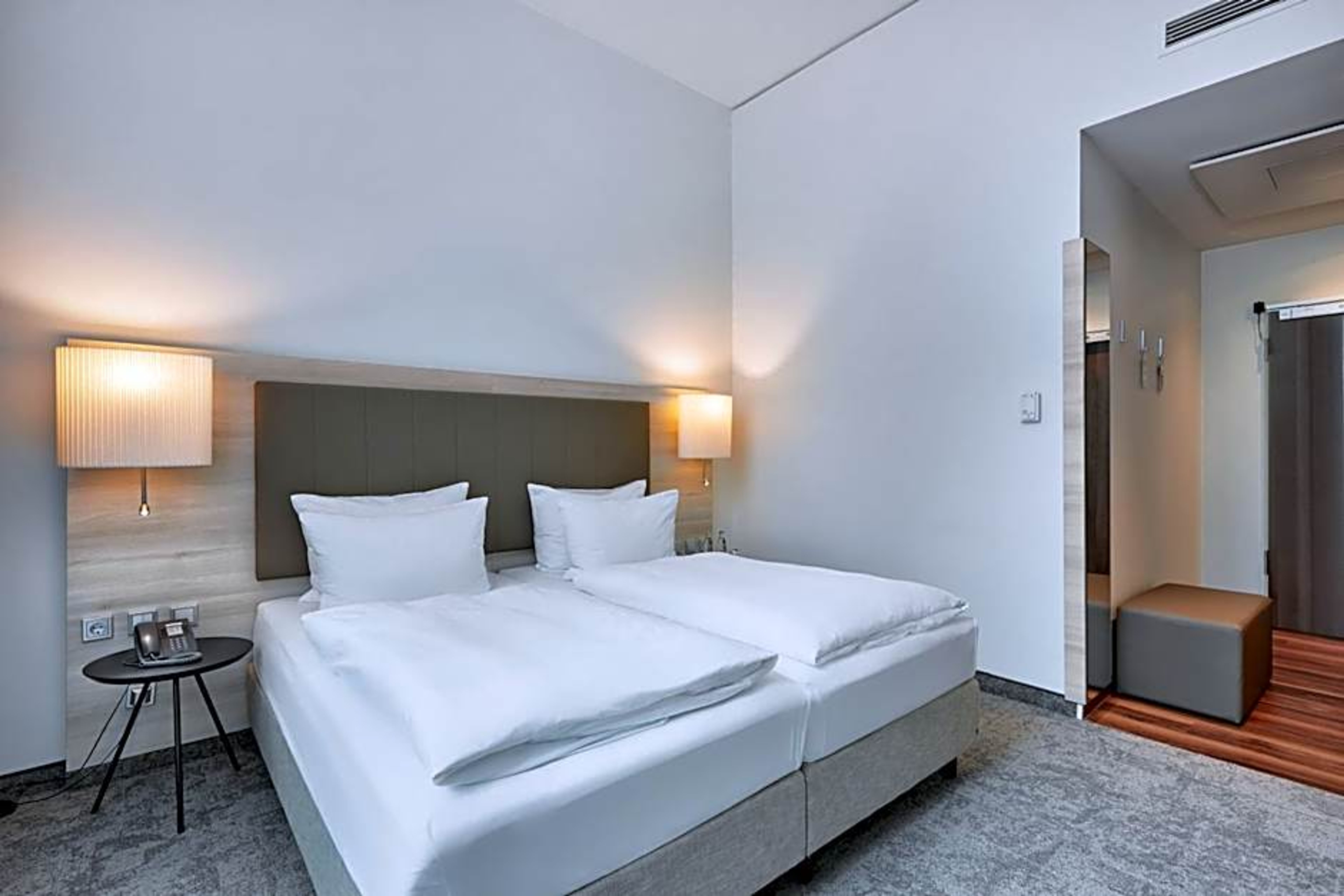 Helles, modernes Hotelzimmer mit zwei getrennten Einzelbetten, weissen Bettwäsche, Nachttischlampen und schlichtem, gemütlichem Ambiente. Helles, modernes Hotelzimmer mit zwei getrennten Einzelbetten, weissen Bettwäsche, Nachttischlampen und schlichtem, gemütlichem Ambiente.