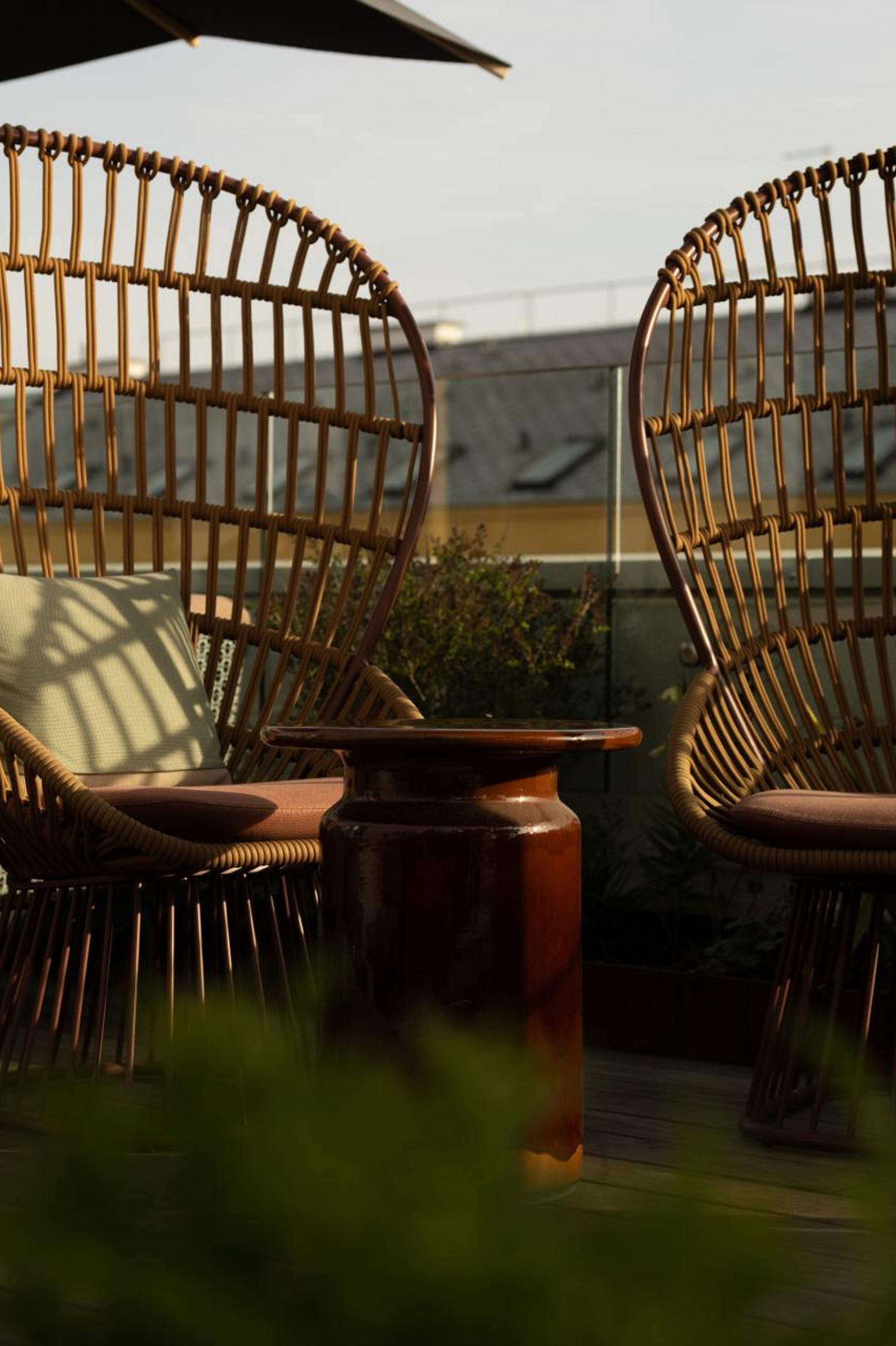 Zwei Rattanstühle mit gemütlichen Kissen stehen auf einer sonnigen Dachterrasse, umgeben von Pflanzen, ideal für entspannte Momente mit Ausblick.