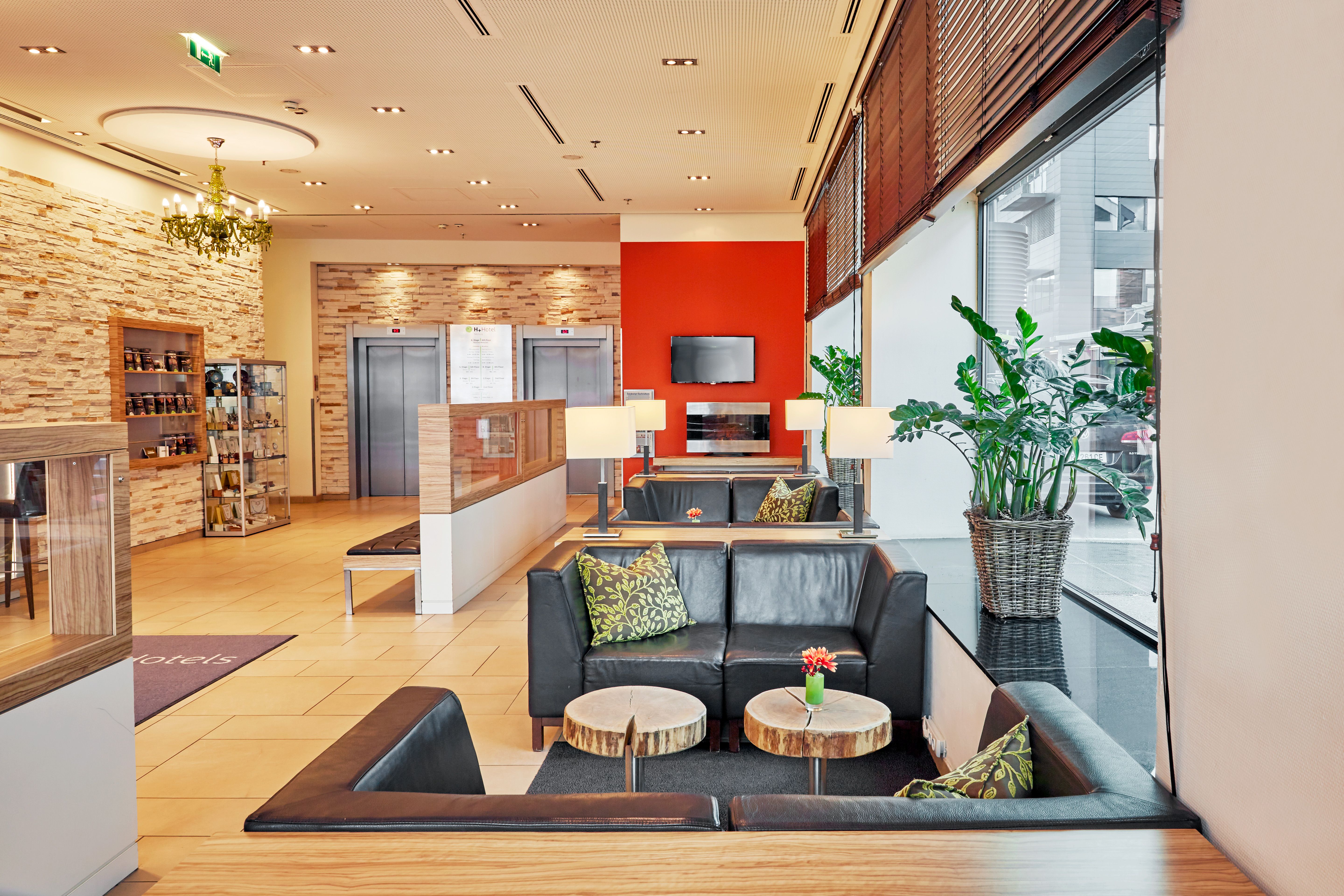 Moderne Hotellobby mit bequemen schwarzen Ledersofas, kleinen Holztischen, großen Fenstern für Tageslicht und grünen Pflanzen, die eine freundliche und einladende Atmosphäre schaffen. Warme Beleuchtung und dezente Dekoration sorgen für Wohlfühlambiente.