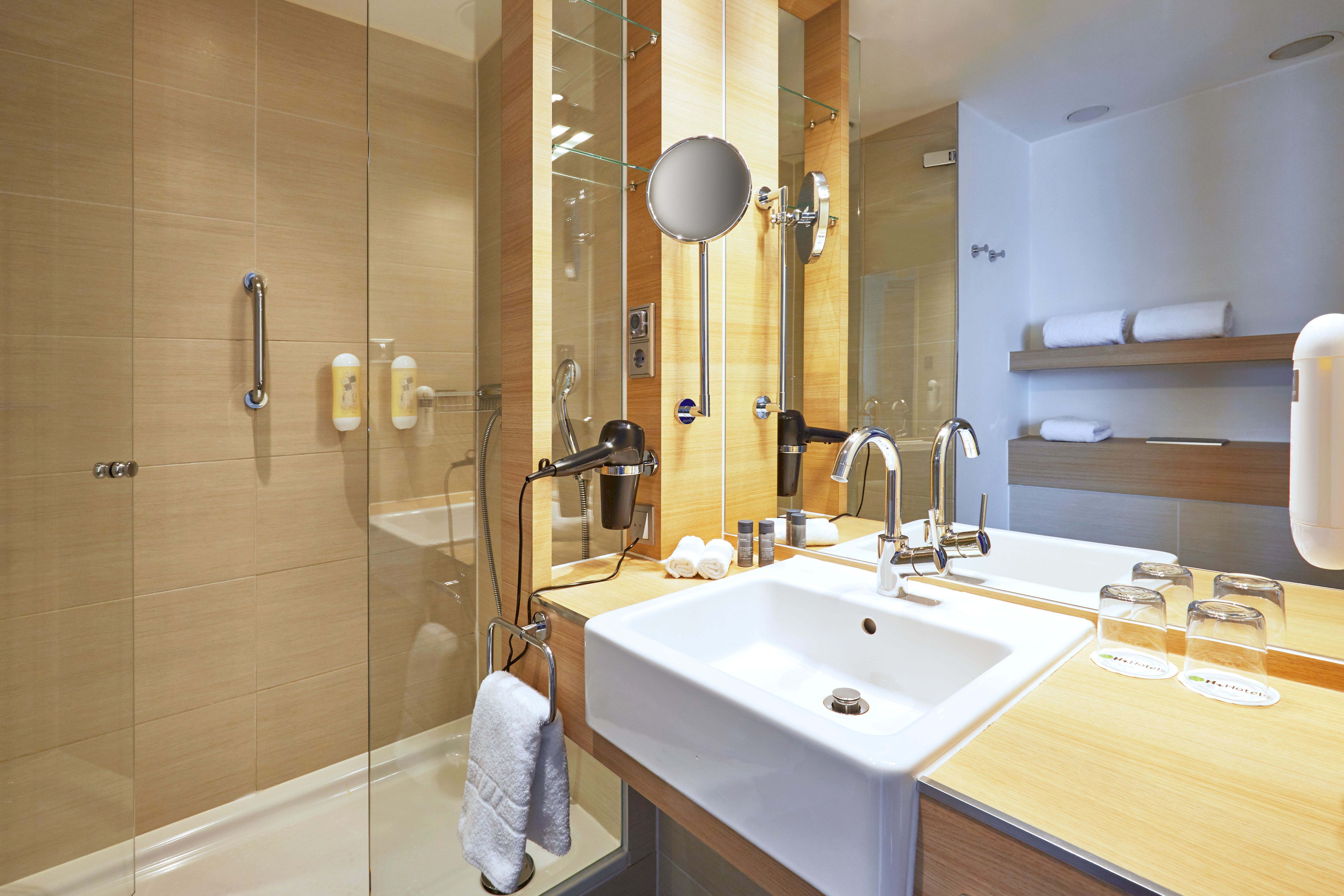 Modernes, helles Badezimmer mit Glasdusche, großzügigem Waschbecken, großen Spiegeln und frischen Handtüchern, das Sauberkeit und Komfort für entspannte Momente bietet.