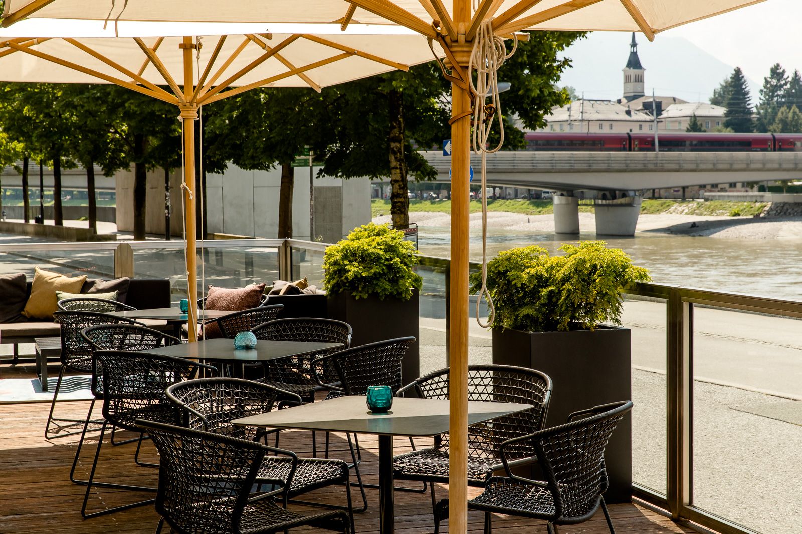 Designhotel Salzburg Mirabell Motel One Außenbereich mit mehreren Sitzgelegenheiten und Blick auf Fluss