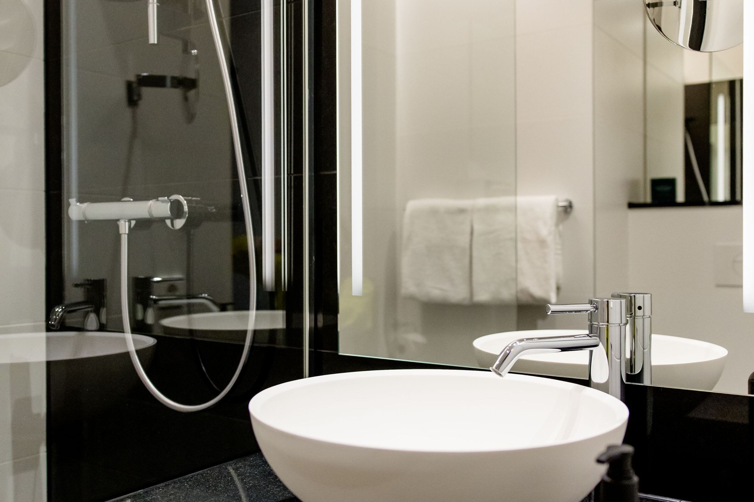 Hotel Wien Donau City Motel One Bad mit Blick auf die Dusche, ein Waschbecken sowie einen großen Spiegel