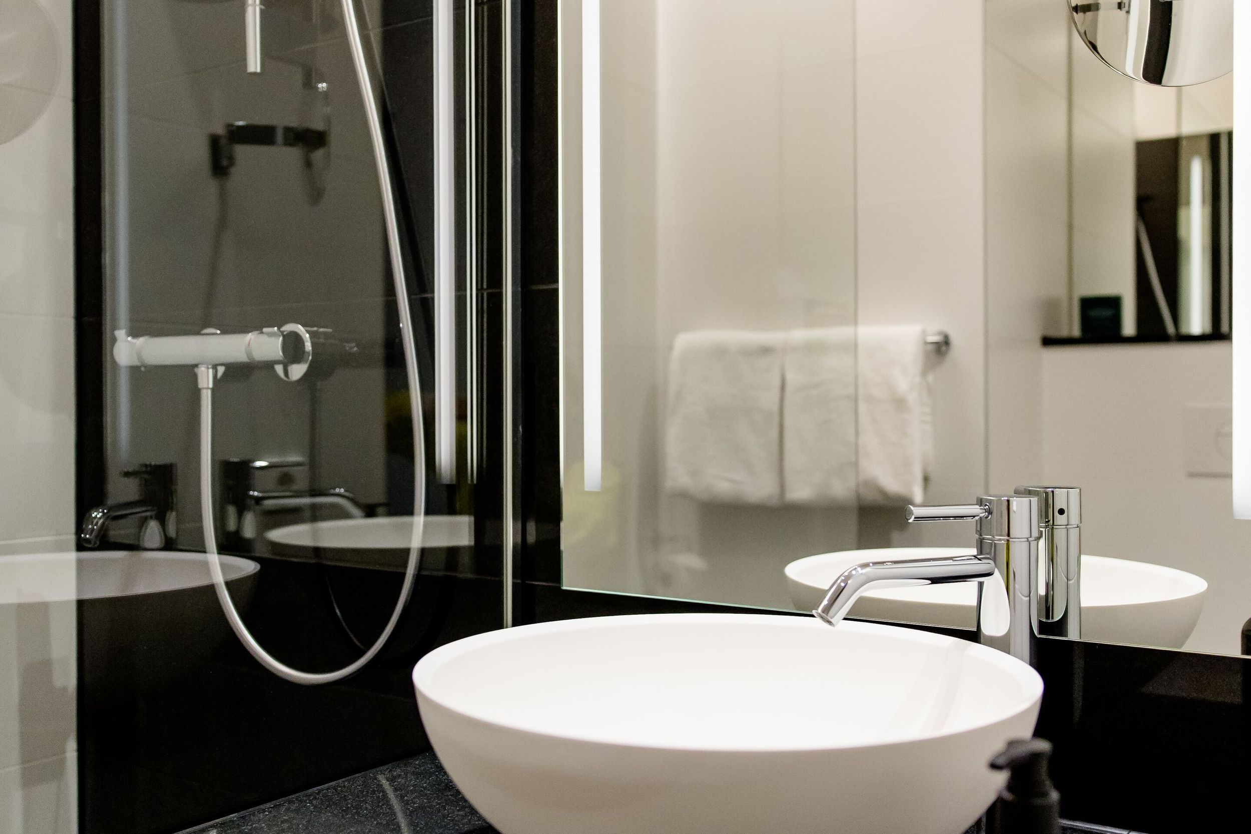 Hotel Wien Donau City Motel One Bad mit Blick auf die Dusche, ein Waschbecken sowie einen großen Spiegel