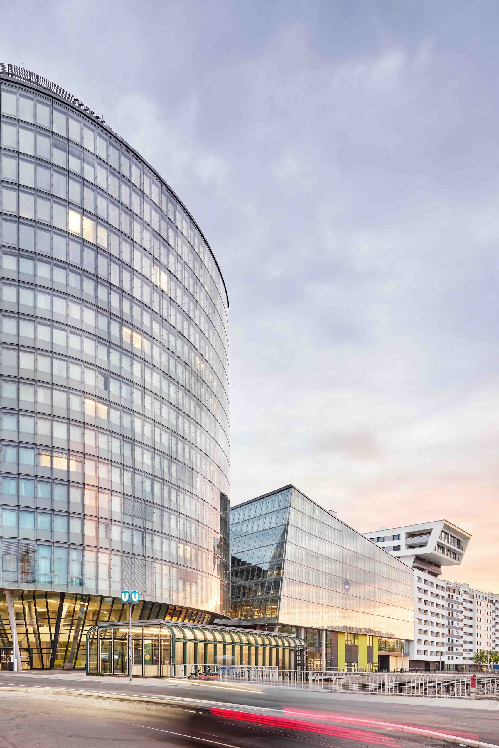 Modernes, elegantes Hotelgebäude mit geschwungener Glasfassade, das städtisches, urbanes Flair vermittelt. Ideal für Geschäftsreisende und Stadtentdecker, zentrale Lage mit guter Anbindung bei Sonnenuntergang.