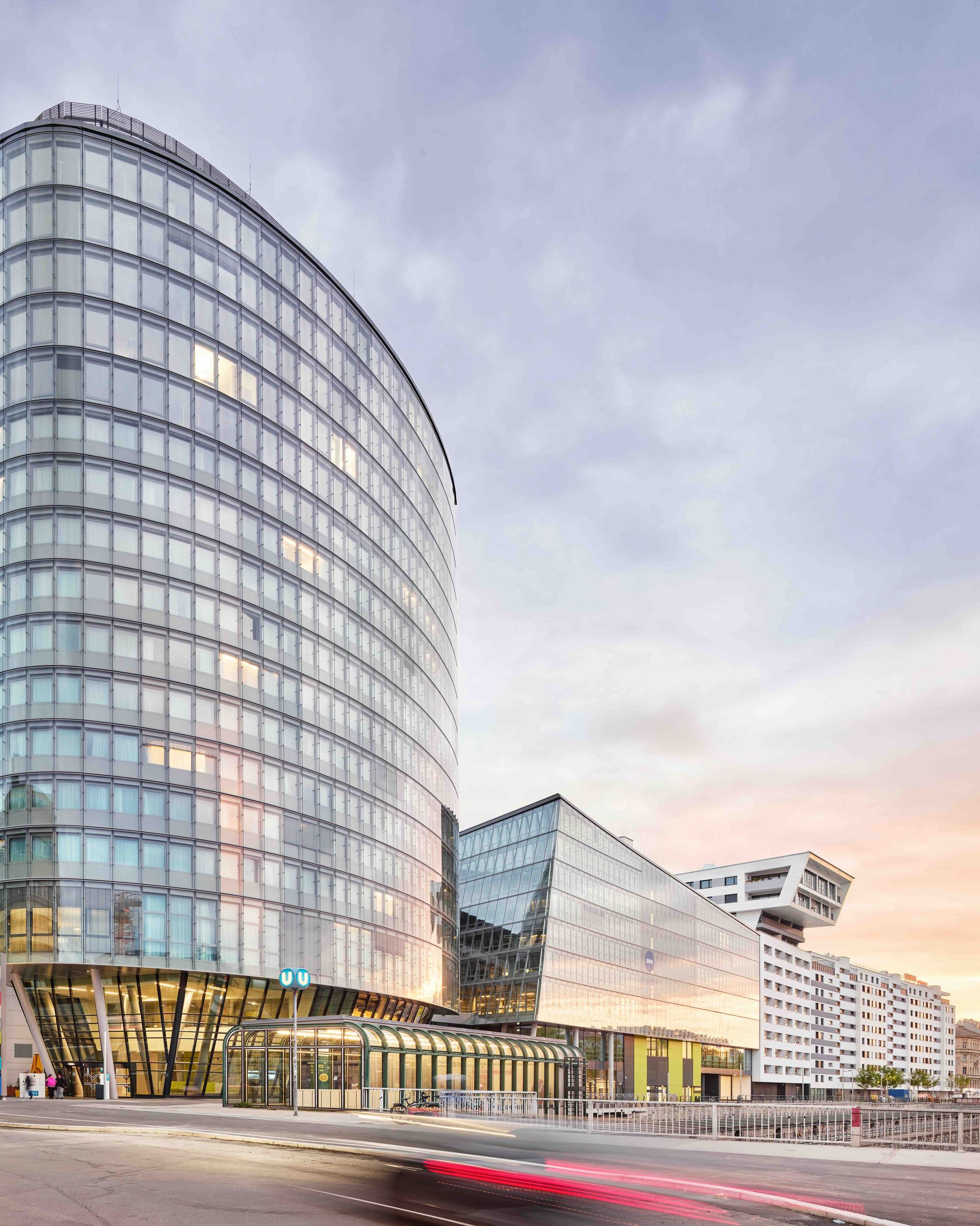 Modernes, elegantes Hotelgebäude mit geschwungener Glasfassade, das städtisches, urbanes Flair vermittelt. Ideal für Geschäftsreisende und Stadtentdecker, zentrale Lage mit guter Anbindung bei Sonnenuntergang.
