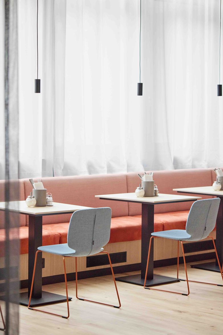 Moderner Essbereich mit hellen Stühlen, rosafarbenem Sofa und kleinen Tischen vor lichtdurchlässigen Vorhängen, schafft eine einladende und ruhige Atmosphäre zum Speisen.