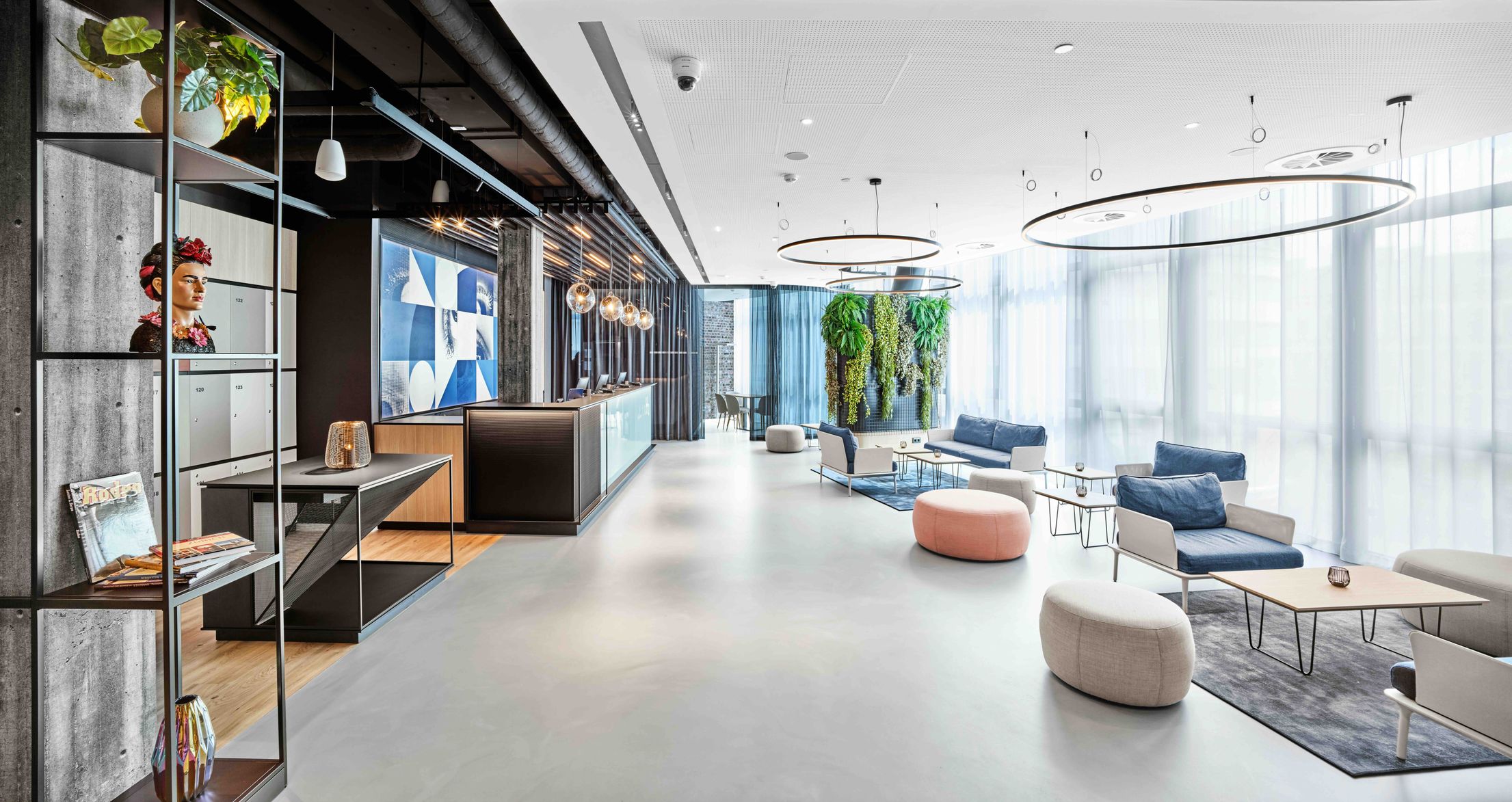 Moderne Hotellobby mit stilvoller Einrichtung, großen Fenstern, natürlichem Licht, gemütlichen Sitzbereichen und grünen Pflanzen an der Wand für eine einladende Atmosphäre.