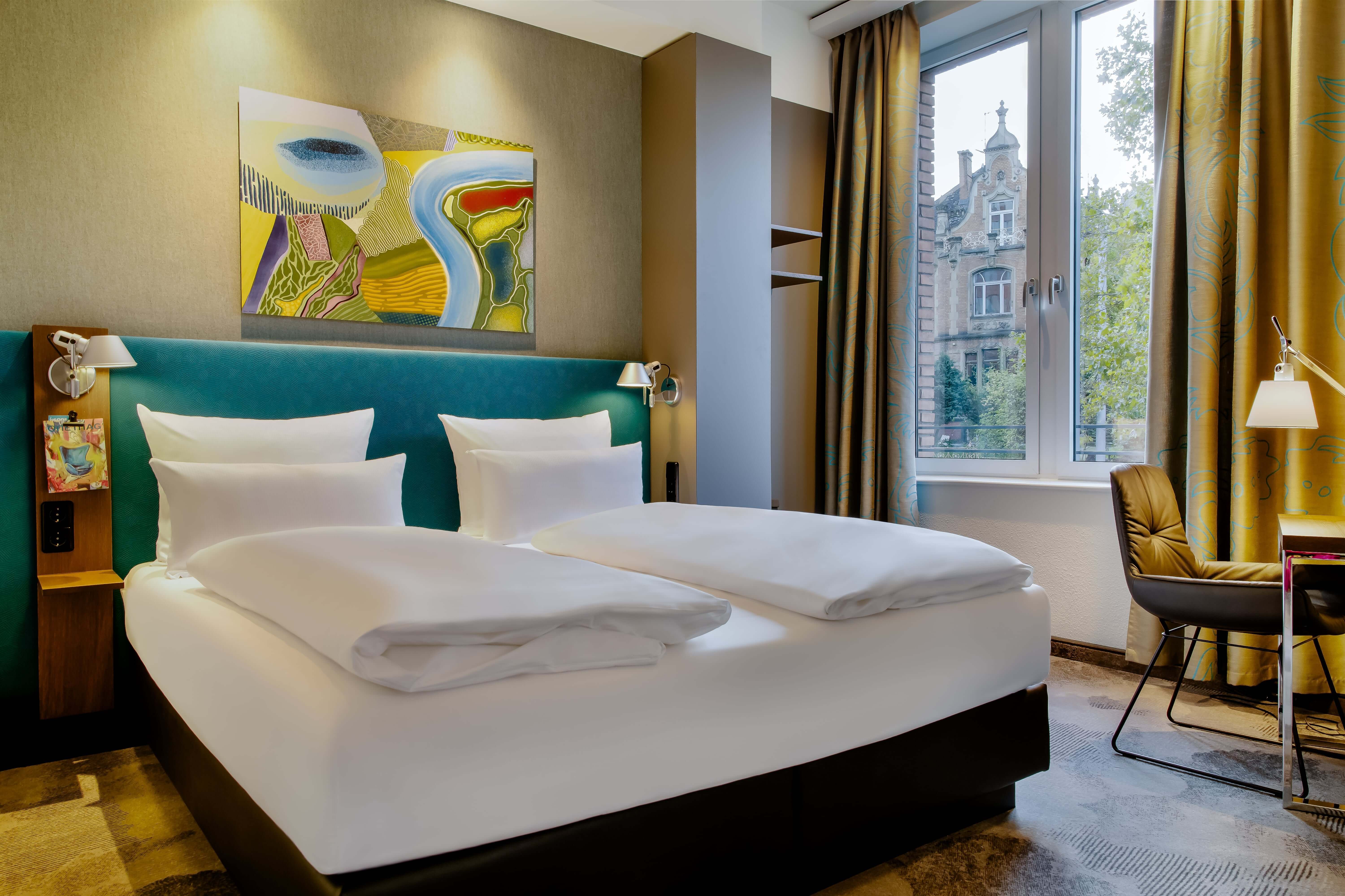 Hotel Wiesbaden Motel One großes Doppelbett mit hellem Fenster und Sessel